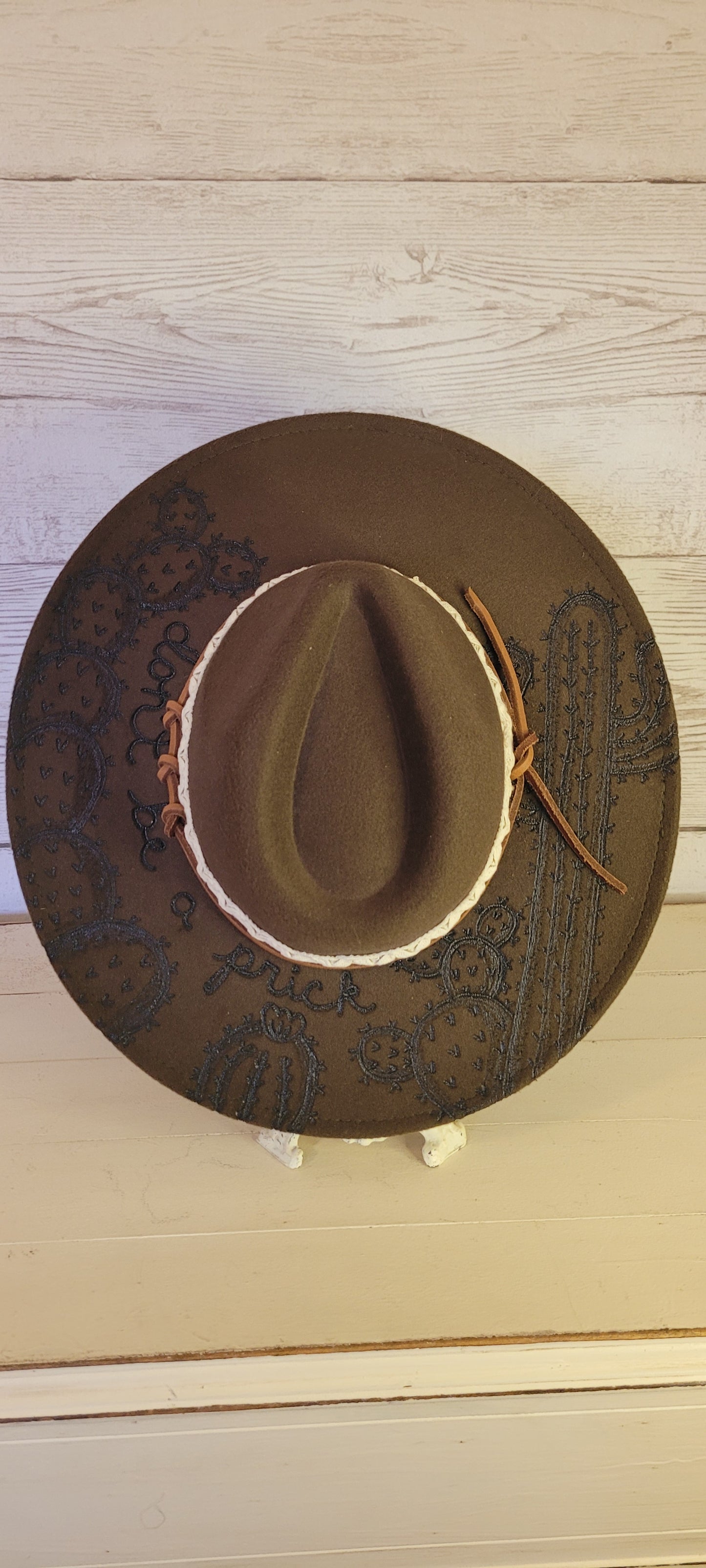 Features "don't be a prick", cactus & saguaro engraving Natural lace ribbon & leather band Felt hat Flat brim 65% polyester and 35% cotton Ribbon drawstring for hat size adjustment Head Circumference: 24" Crown Height: 5" Brim Length: 15.75" Brim Width: 14.5" Branded & numbered inside crown Custom designed by Kayla