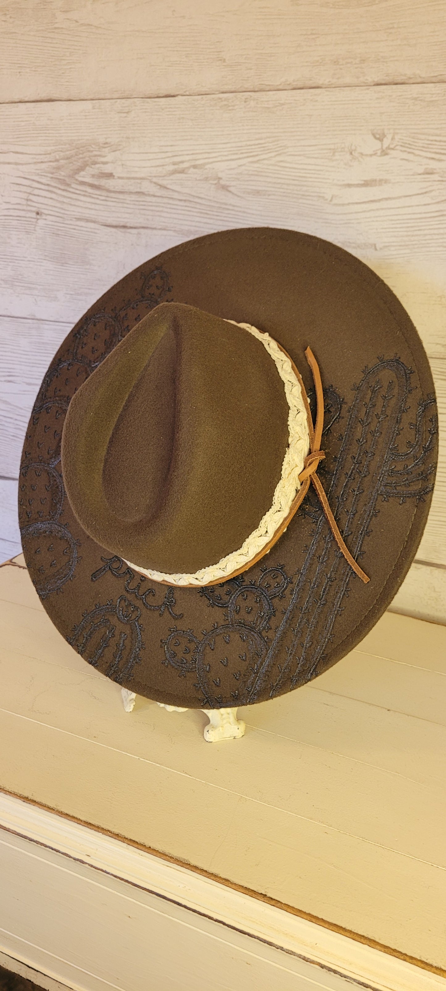 Features "don't be a prick", cactus & saguaro engraving Natural lace ribbon & leather band Felt hat Flat brim 65% polyester and 35% cotton Ribbon drawstring for hat size adjustment Head Circumference: 24" Crown Height: 5" Brim Length: 15.75" Brim Width: 14.5" Branded & numbered inside crown Custom designed by Kayla