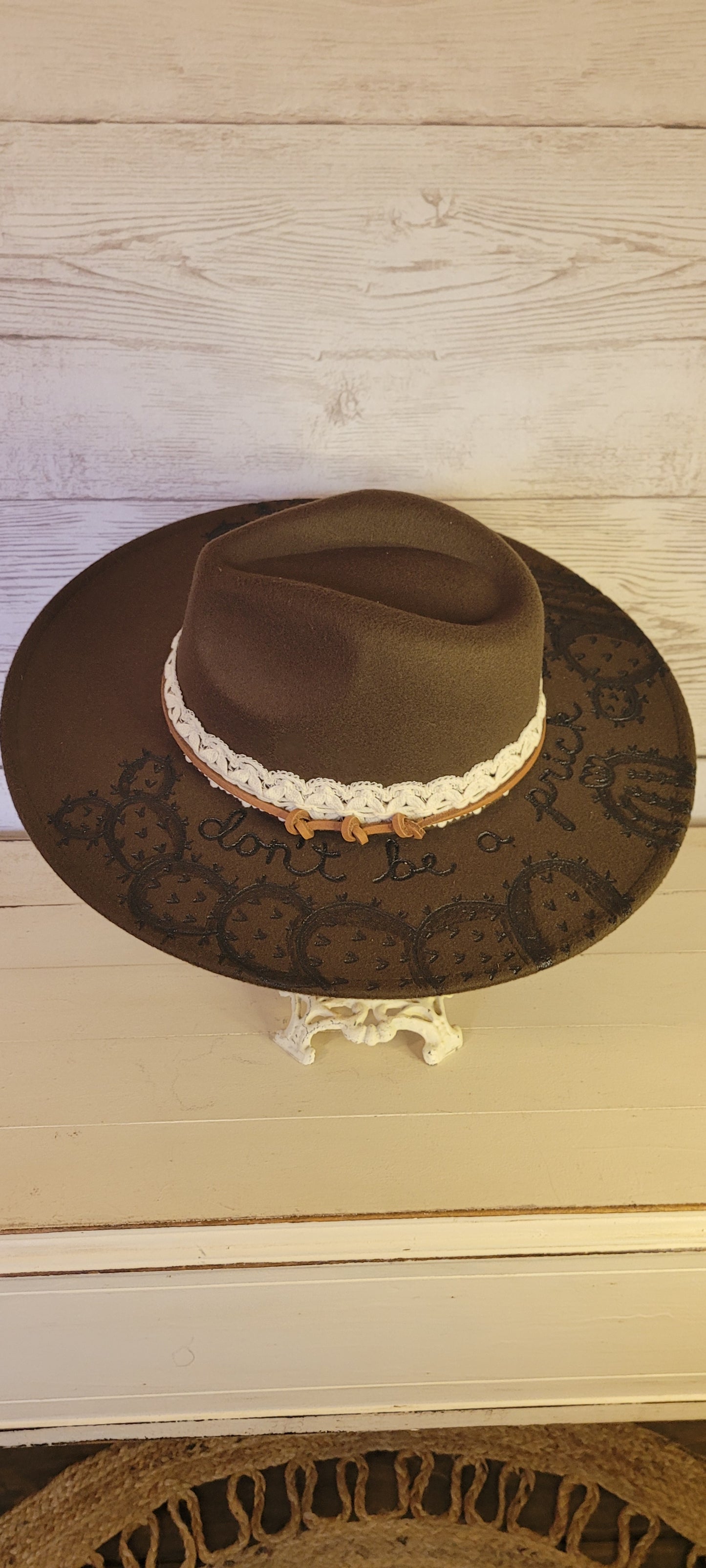 Features "don't be a prick", cactus & saguaro engraving Natural lace ribbon & leather band Felt hat Flat brim 65% polyester and 35% cotton Ribbon drawstring for hat size adjustment Head Circumference: 24" Crown Height: 5" Brim Length: 15.75" Brim Width: 14.5" Branded & numbered inside crown Custom designed by Kayla