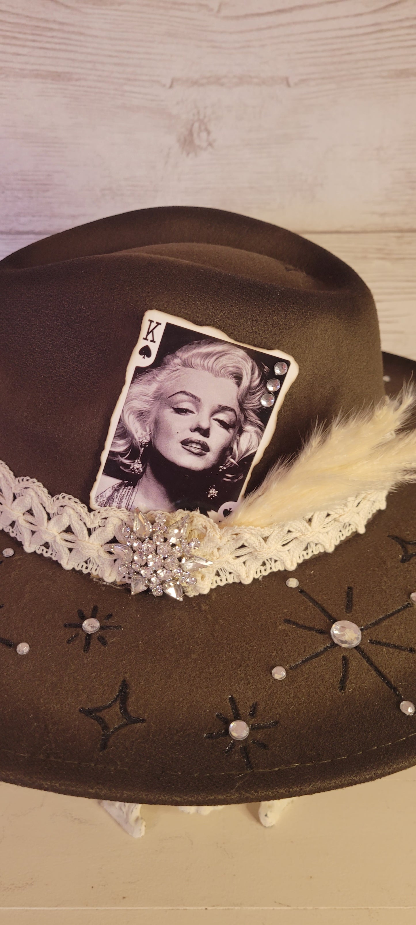 Features engraved stars & diamonds Rhinestone details throughout, pampas, crystal brooch, & playing card Felt hat Flat brim 65% polyester and 35% cotton Ribbon drawstring for hat size adjustment Head Circumference: 24" Crown Height: 5" Brim Length: 15.75" Brim Width: 14.5" Branded & numbered inside crown Custom designed by Kayla