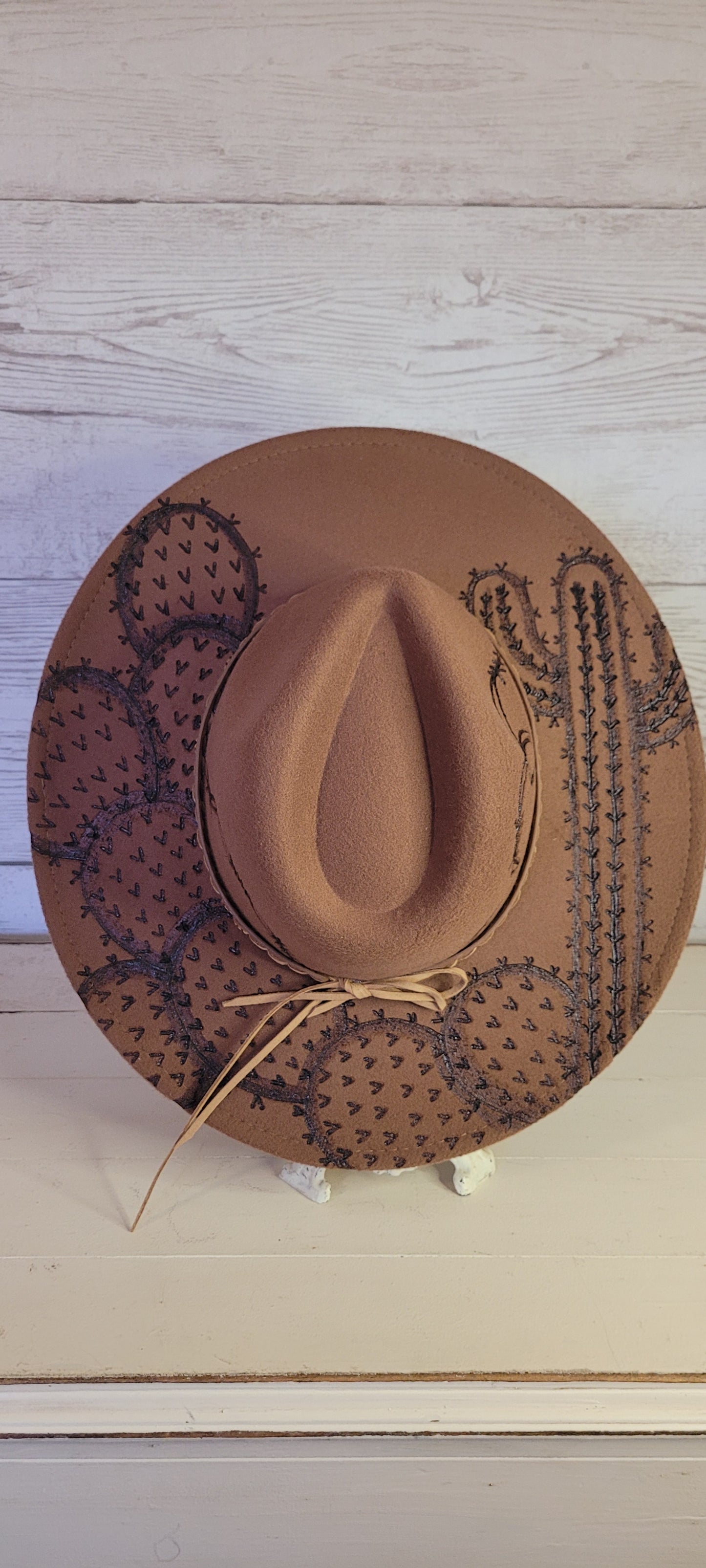 Features barbwire, cactus & saguaro Natural lace ribbon & leather band Felt hat Flat brim 100% polyester Ribbon drawstring for hat size adjustment Head Circumference: 24" Crown Height: 5" Brim Length: 15.75" Brim Width: 14.5" Branded & numbered inside crown Custom engraved by Kayla