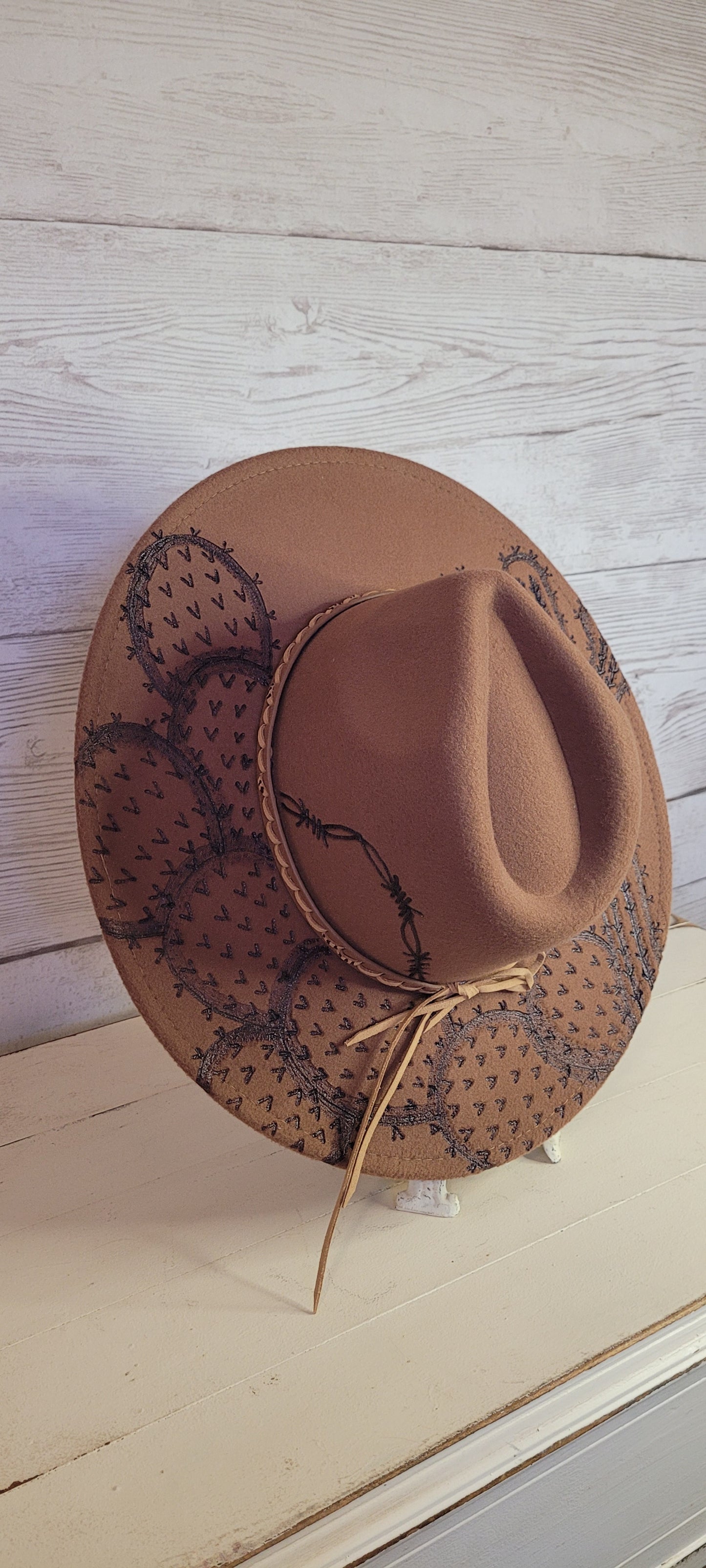 Features barbwire, cactus & saguaro Natural lace ribbon & leather band Felt hat Flat brim 100% polyester Ribbon drawstring for hat size adjustment Head Circumference: 24" Crown Height: 5" Brim Length: 15.75" Brim Width: 14.5" Branded & numbered inside crown Custom engraved by Kayla