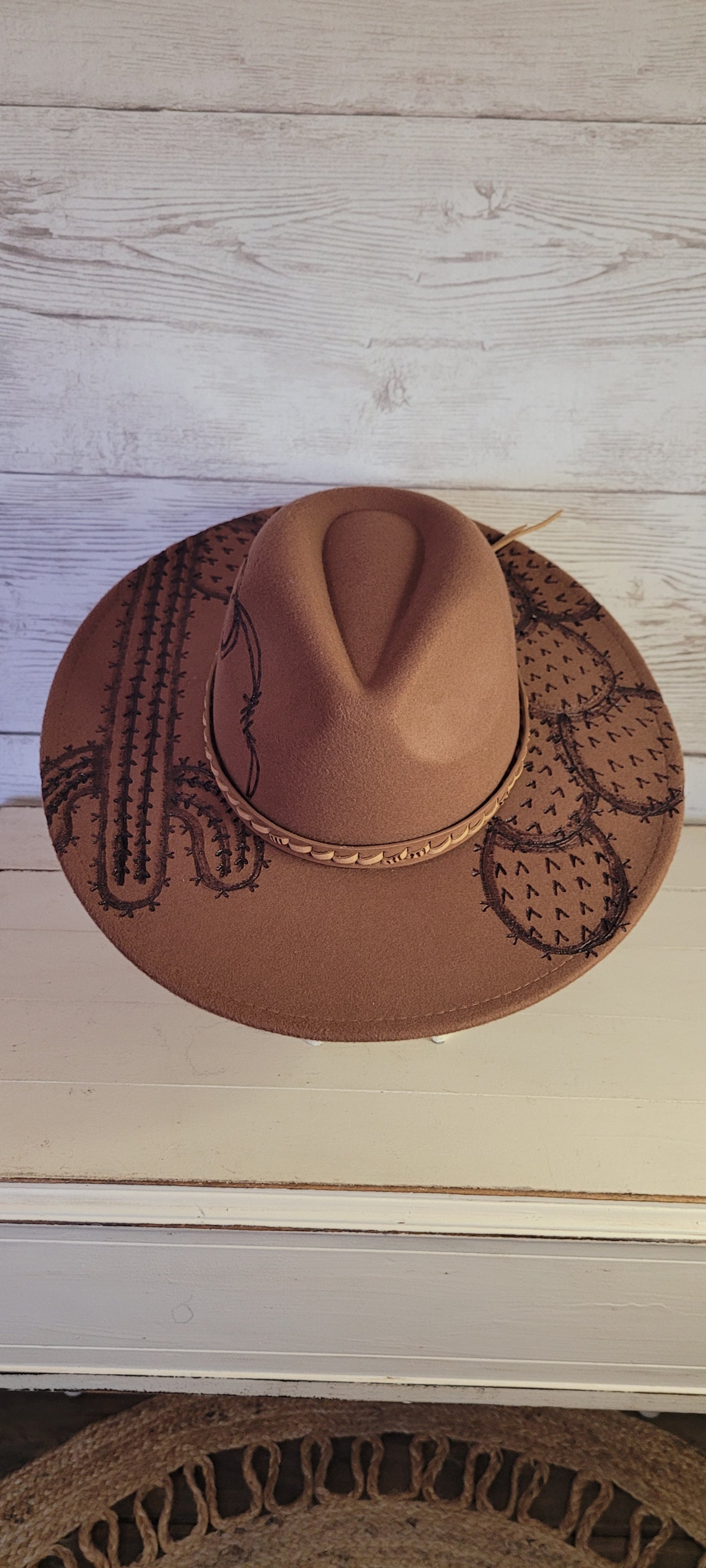 Features barbwire, cactus & saguaro Natural lace ribbon & leather band Felt hat Flat brim 100% polyester Ribbon drawstring for hat size adjustment Head Circumference: 24" Crown Height: 5" Brim Length: 15.75" Brim Width: 14.5" Branded & numbered inside crown Custom engraved by Kayla