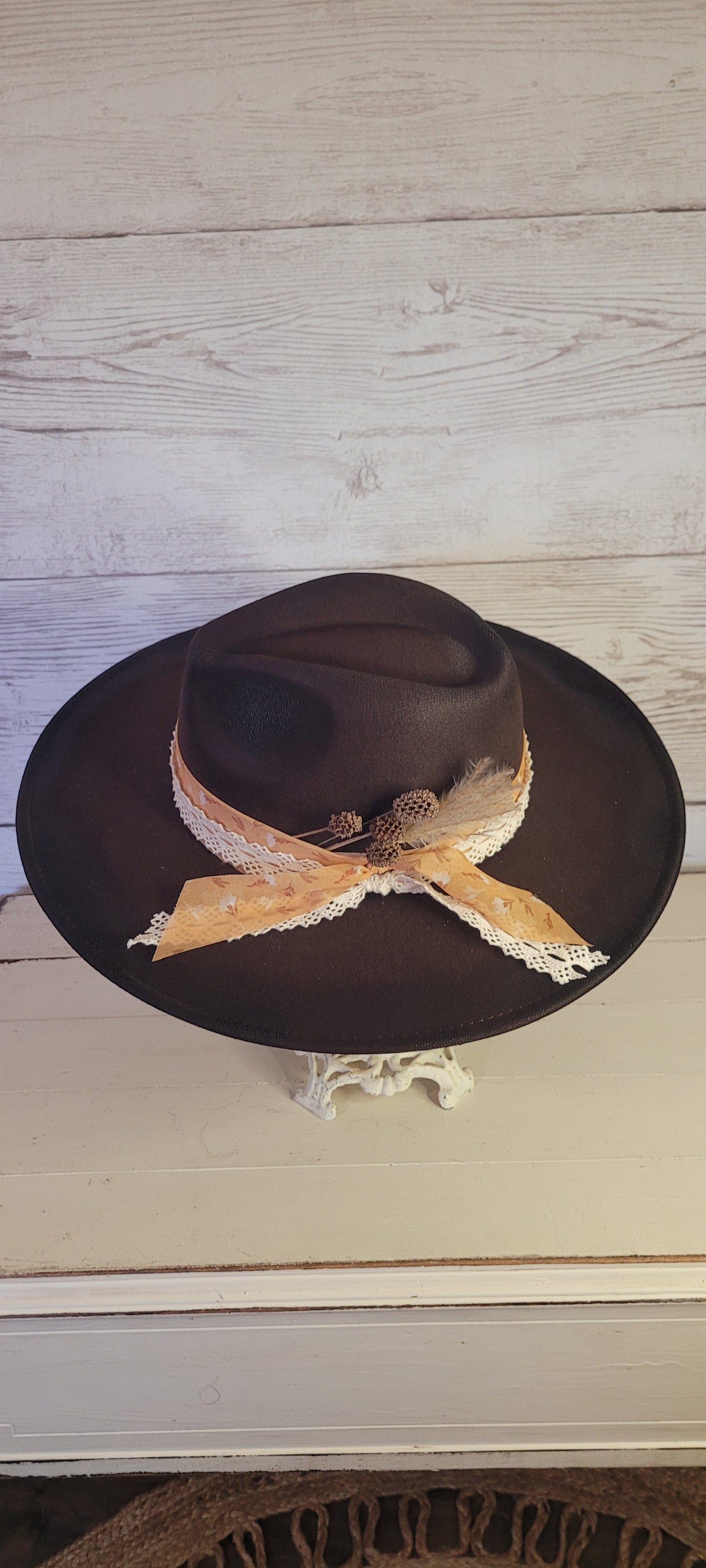 Features natural lace ribbon, sheer mustard ribbon, pine cones, & pampas Felt hat Flat brim 65% polyester and 35% cotton Ribbon drawstring for hat size adjustment Head Circumference: 24" Crown Height: 5" Brim Length: 15.75" Brim Width: 14.5" Branded & numbered inside crown Custom designed by Kayla