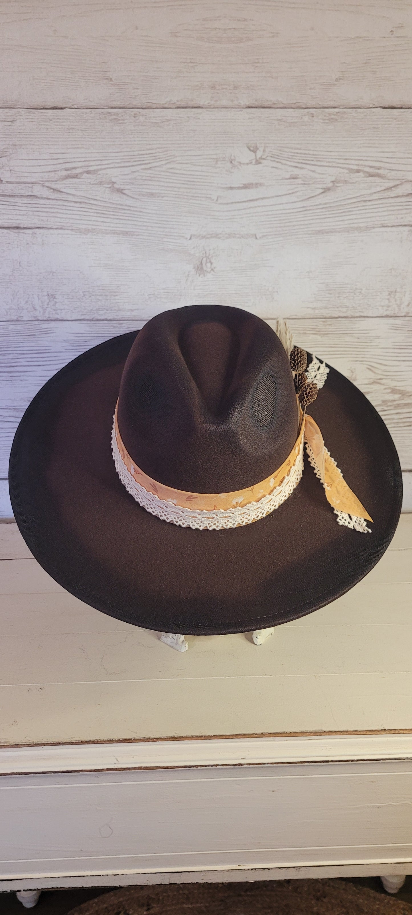 Features natural lace ribbon, sheer mustard ribbon, pine cones, & pampas Felt hat Flat brim 65% polyester and 35% cotton Ribbon drawstring for hat size adjustment Head Circumference: 24" Crown Height: 5" Brim Length: 15.75" Brim Width: 14.5" Branded & numbered inside crown Custom designed by Kayla