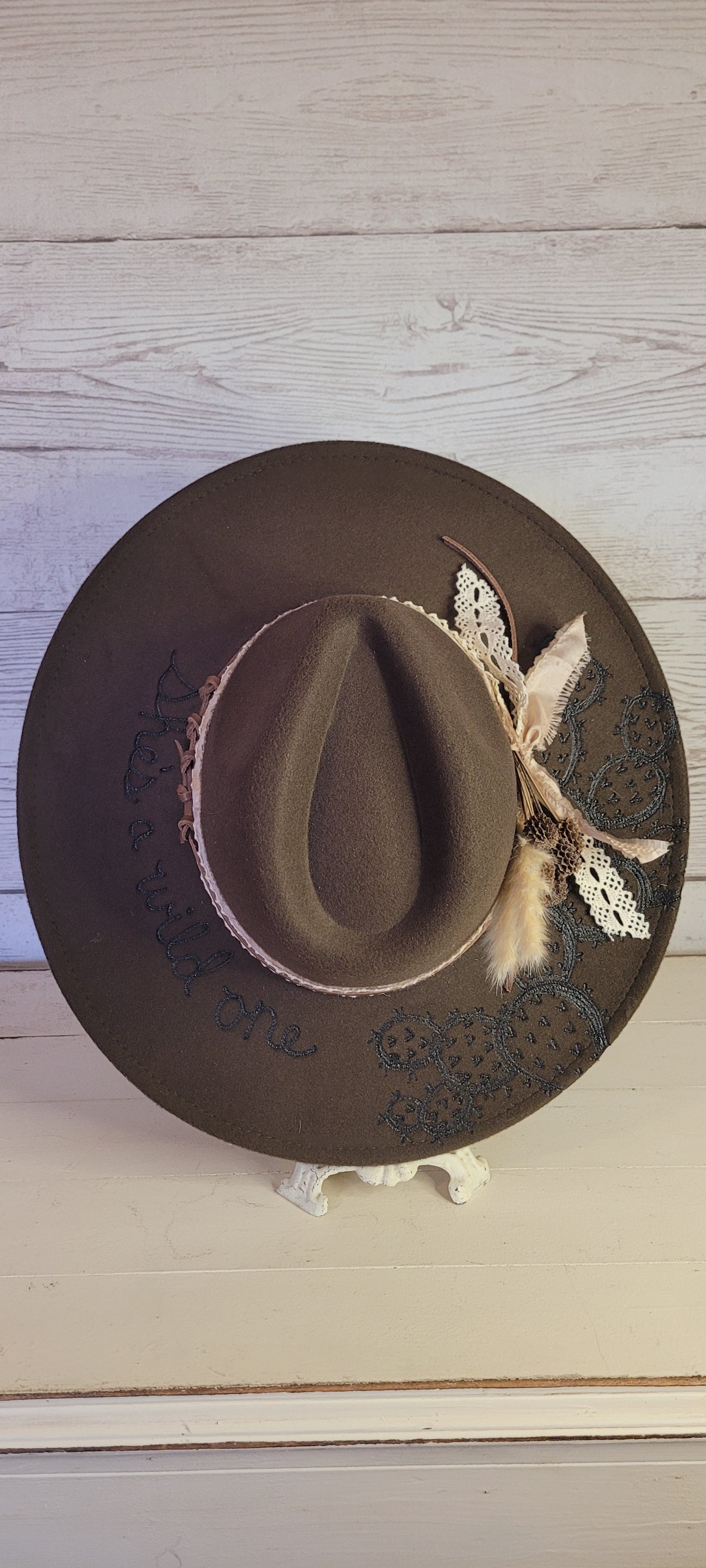 Features "She's a wild one" & cactus engraving Pampas, pine cones, light rose ribbon, natural lace ribbon, leather band Felt hat Flat brim 65% polyester and 35% cotton Ribbon drawstring for hat size adjustment Head Circumference: 24" Crown Height: 5" Brim Length: 15.75" Brim Width: 14.5" Branded & numbered inside crown Custom designed by Kayla