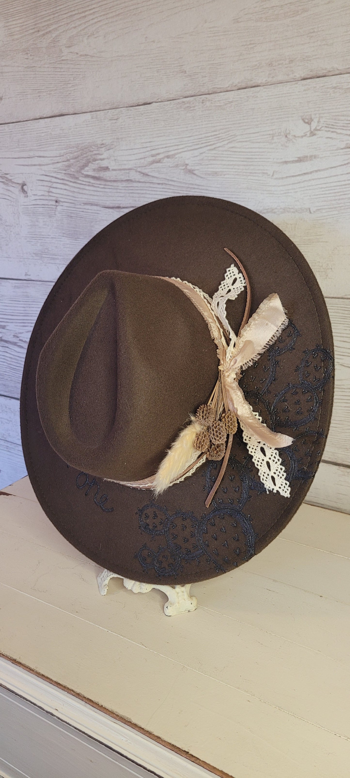 Features "She's a wild one" & cactus engraving Pampas, pine cones, light rose ribbon, natural lace ribbon, leather band Felt hat Flat brim 65% polyester and 35% cotton Ribbon drawstring for hat size adjustment Head Circumference: 24" Crown Height: 5" Brim Length: 15.75" Brim Width: 14.5" Branded & numbered inside crown Custom designed by Kayla