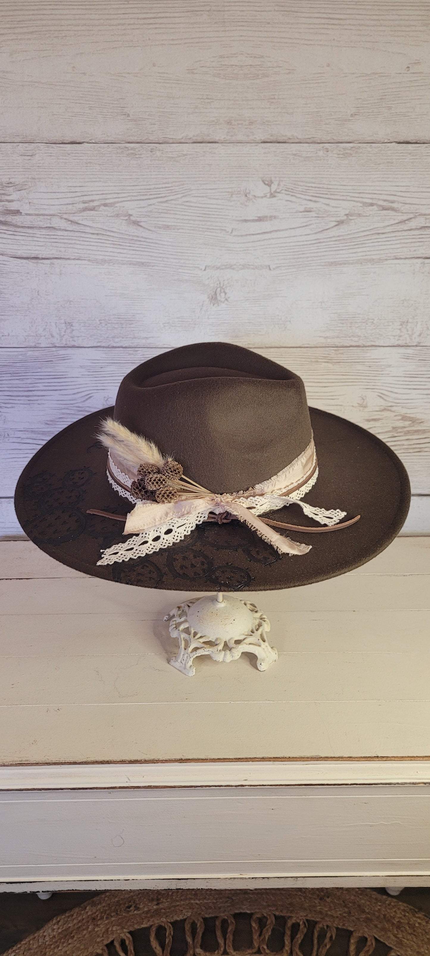 Features "She's a wild one" & cactus engraving Pampas, pine cones, light rose ribbon, natural lace ribbon, leather band Felt hat Flat brim 65% polyester and 35% cotton Ribbon drawstring for hat size adjustment Head Circumference: 24" Crown Height: 5" Brim Length: 15.75" Brim Width: 14.5" Branded & numbered inside crown Custom designed by Kayla