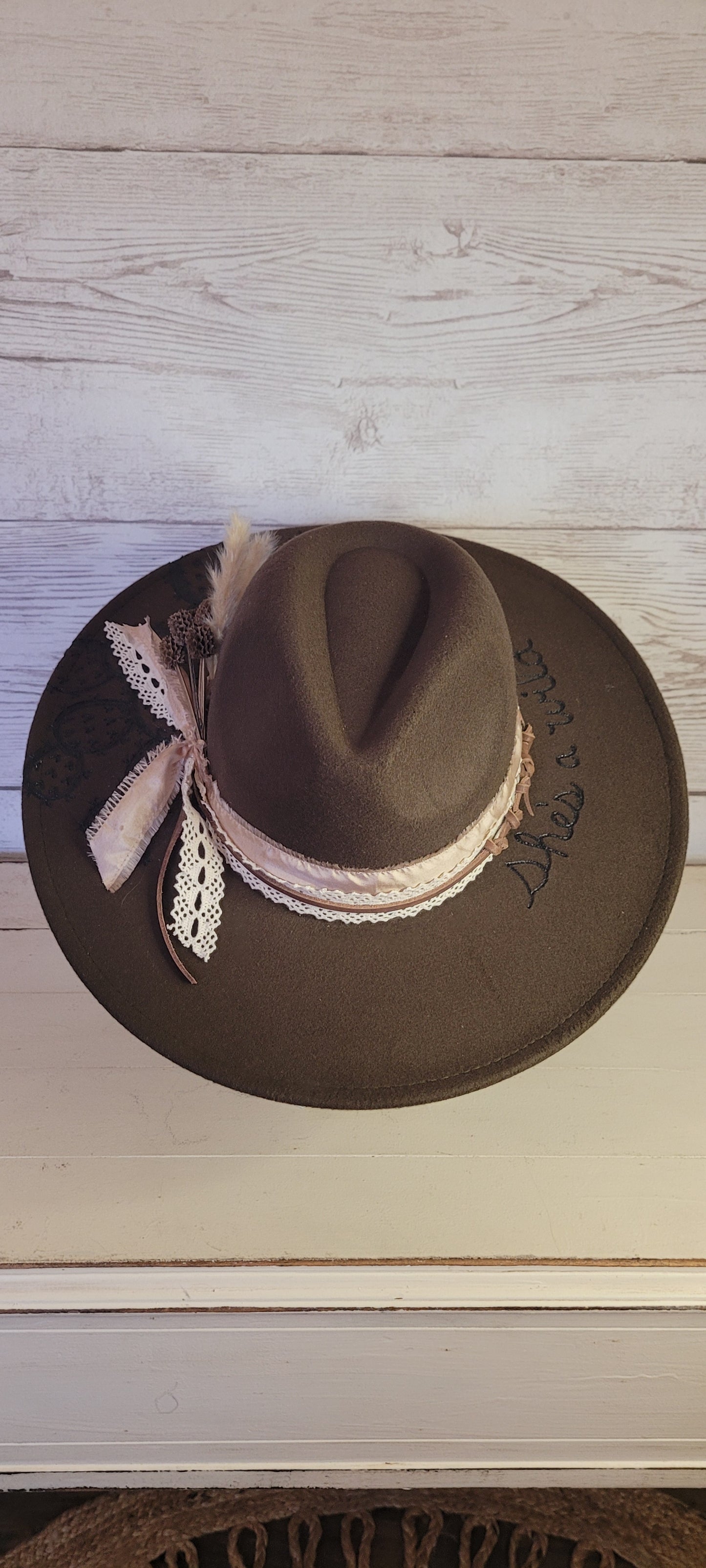 Features "She's a wild one" & cactus engraving Pampas, pine cones, light rose ribbon, natural lace ribbon, leather band Felt hat Flat brim 65% polyester and 35% cotton Ribbon drawstring for hat size adjustment Head Circumference: 24" Crown Height: 5" Brim Length: 15.75" Brim Width: 14.5" Branded & numbered inside crown Custom designed by Kayla