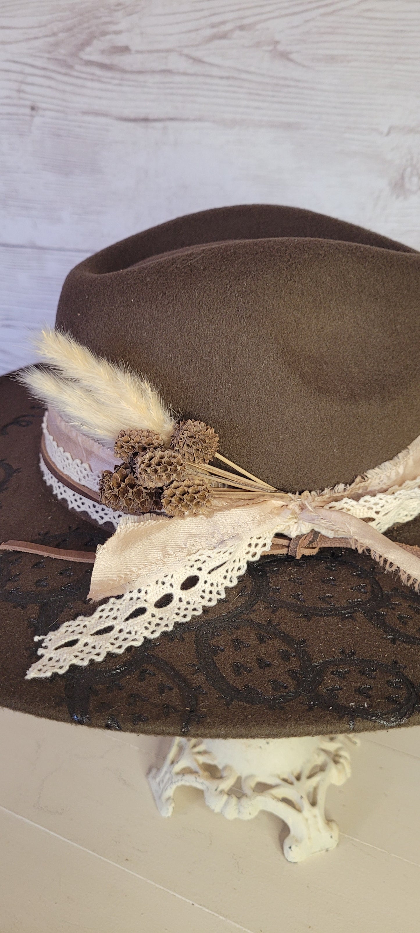 Features "She's a wild one" & cactus engraving Pampas, pine cones, light rose ribbon, natural lace ribbon, leather band Felt hat Flat brim 65% polyester and 35% cotton Ribbon drawstring for hat size adjustment Head Circumference: 24" Crown Height: 5" Brim Length: 15.75" Brim Width: 14.5" Branded & numbered inside crown Custom designed by Kayla