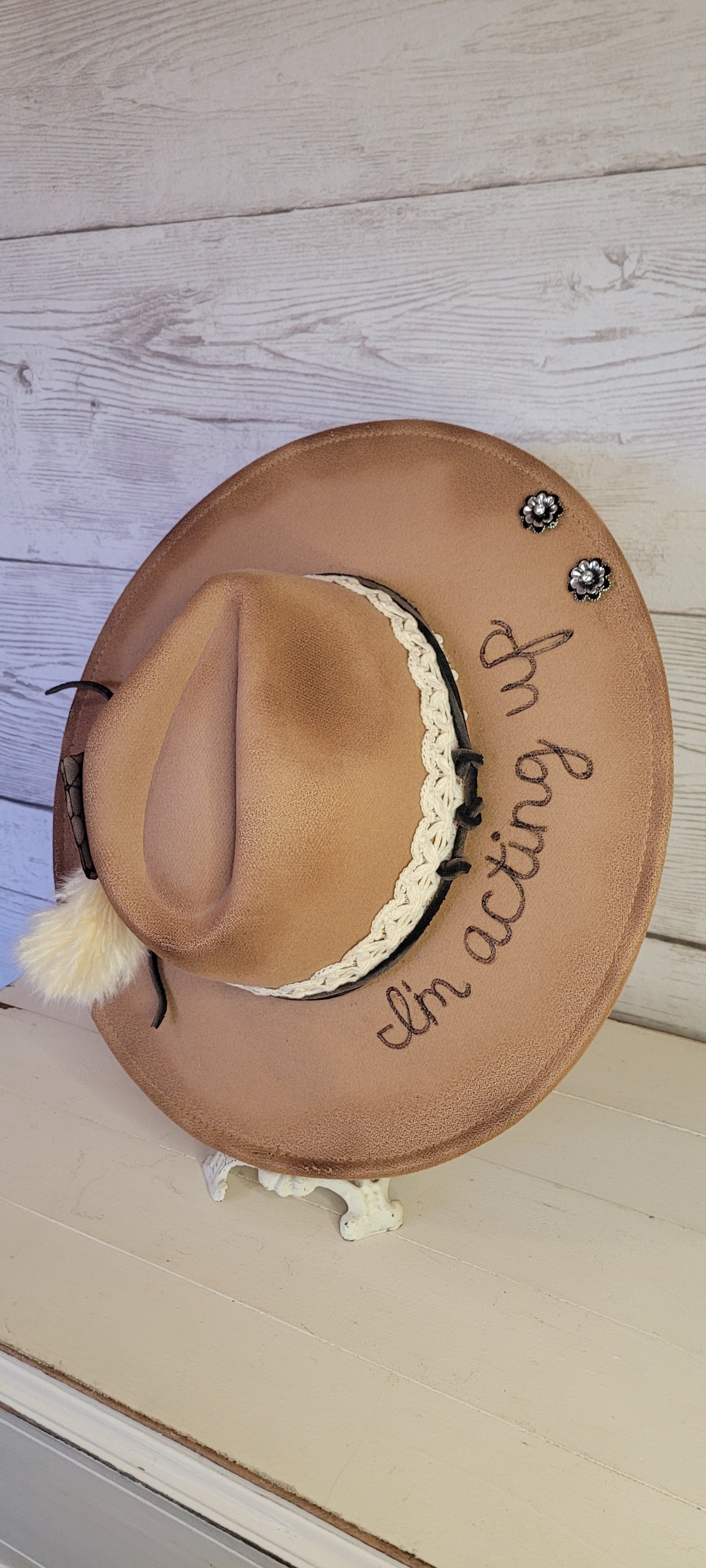 Features "I'm acting up" engraving Lace ribbon, leather band, pampas, rhinestone brooches, playing card Felt hat Flat brim 100% polyester Ribbon drawstring for hat size adjustment Head Circumference: 24" Crown Height: 5" Brim Length: 15.75" Brim Width: 14.5" Branded & numbered inside crown Custom burned & engraved by Kayla