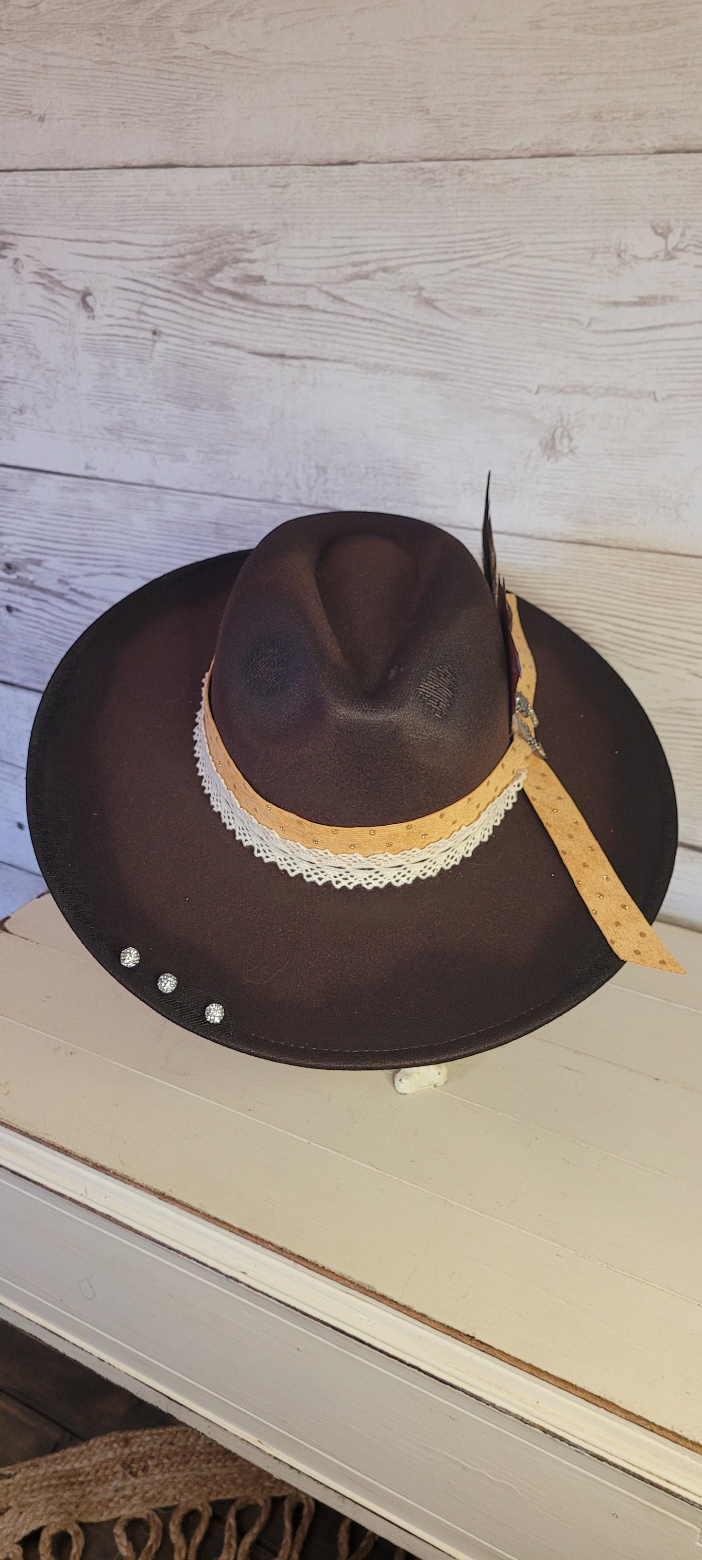 Features natural lace ribbon, corduroy ribbon, feather, playing cards, pistol brooch, & rhinestone beads Felt hat Flat brim 65% polyester and 35% cotton Ribbon drawstring for hat size adjustment Head Circumference: 24" Crown Height: 5" Brim Length: 15.75" Brim Width: 14.5" Branded & numbered inside crown Custom designed by Kayla