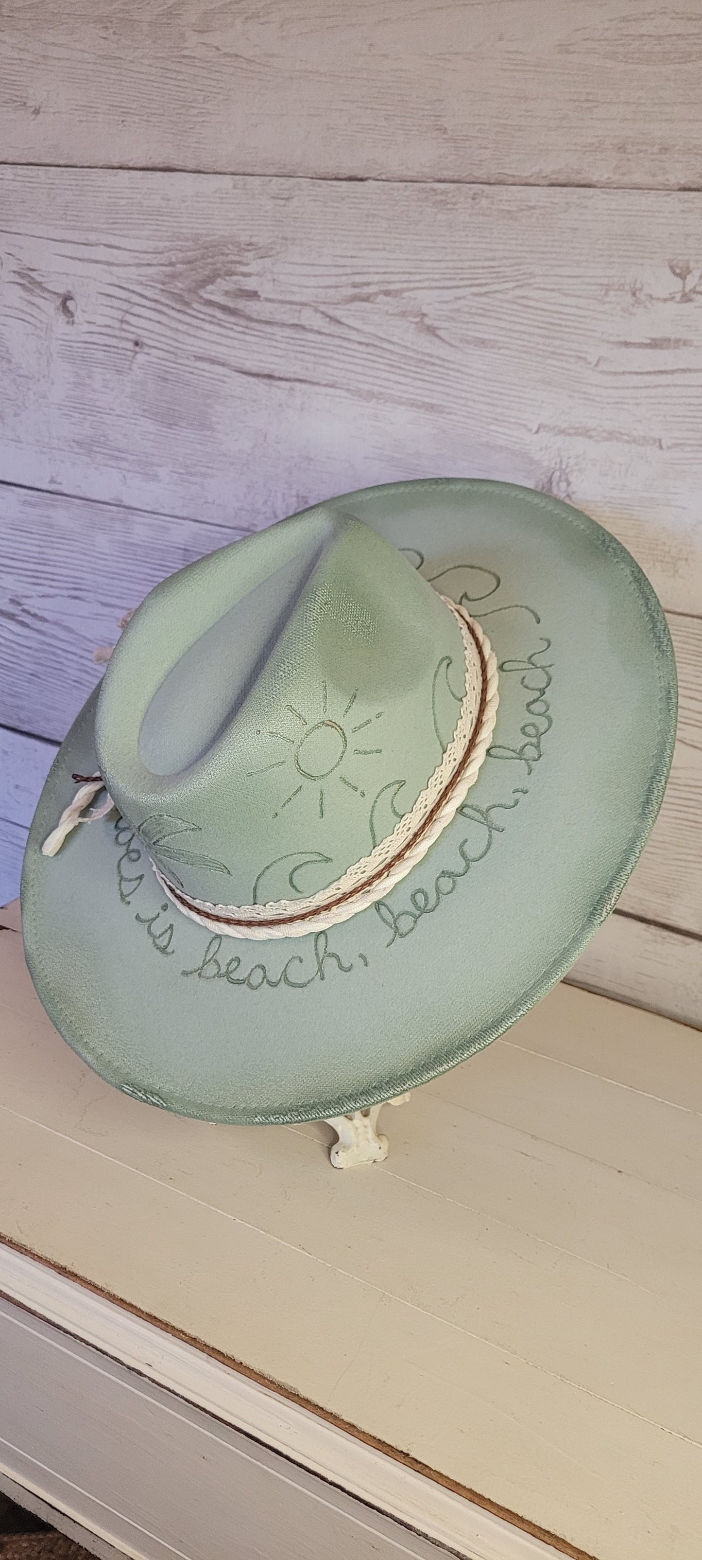 Features sunshine, palm trees, waves & "all she does is beach, beach, beach" engraved Lace ribbon, brown cord, & natural gauze rope Felt hat Flat brim 65% polyester and 35% cotton Ribbon drawstring for hat size adjustment Head Circumference: 24" Crown Height: 5" Brim Length: 15.75" Brim Width: 14.5" Branded & numbered inside crown Custom burned & engraved by Kayla