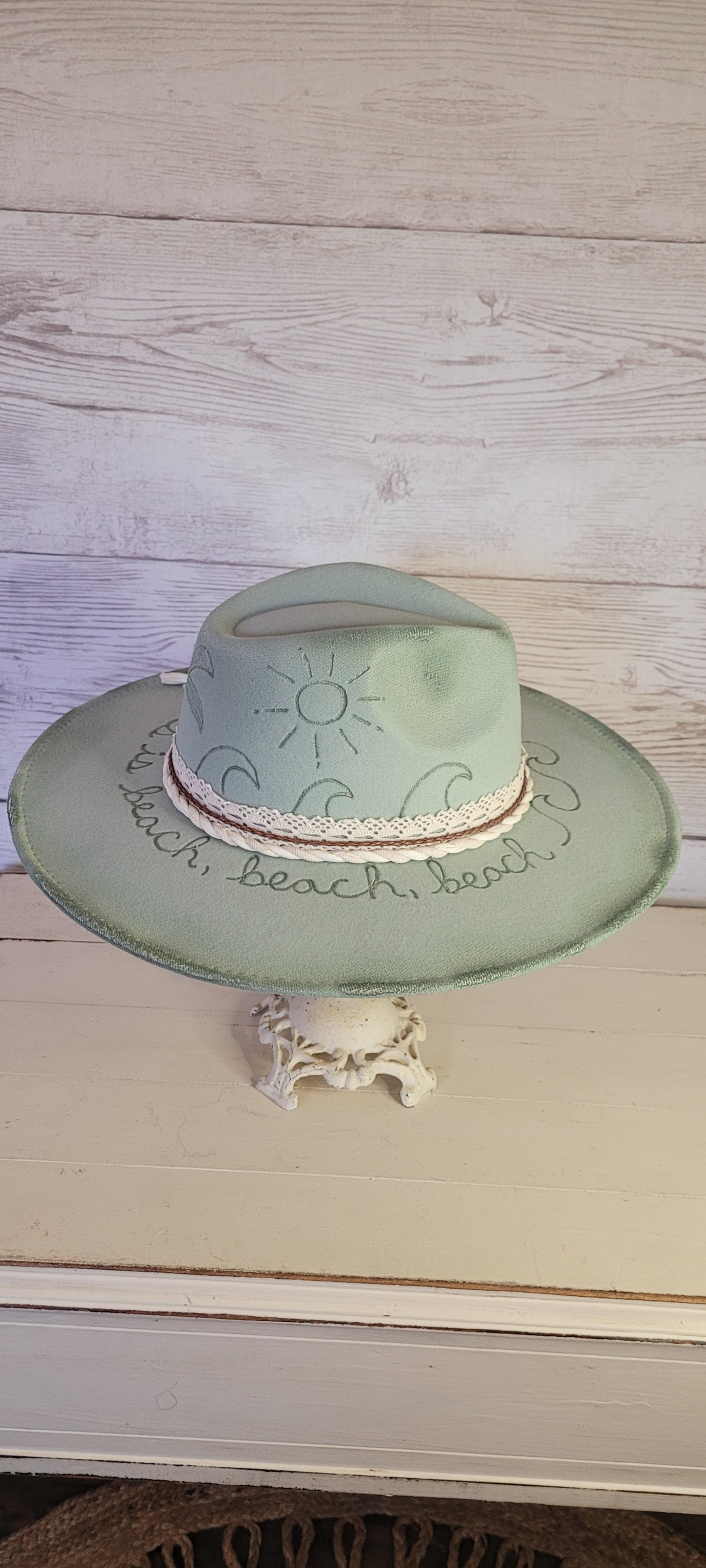Features sunshine, palm trees, waves & "all she does is beach, beach, beach" engraved Lace ribbon, brown cord, & natural gauze rope Felt hat Flat brim 65% polyester and 35% cotton Ribbon drawstring for hat size adjustment Head Circumference: 24" Crown Height: 5" Brim Length: 15.75" Brim Width: 14.5" Branded & numbered inside crown Custom burned & engraved by Kayla