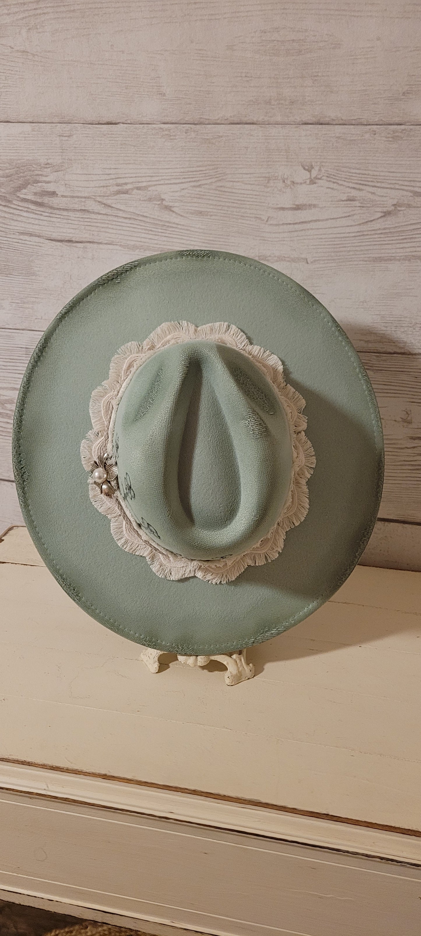 Features flowers engraved Wavy frayed ribbon, natural cord, rhinestones & metal pearl brooch Felt hat Flat brim 100% polyester Ribbon drawstring for hat size adjustment Head Circumference: 24" Crown Height: 5" Brim Length: 15.75" Brim Width: 14.5" Branded & numbered inside crown Custom burned & engraved by Kayla