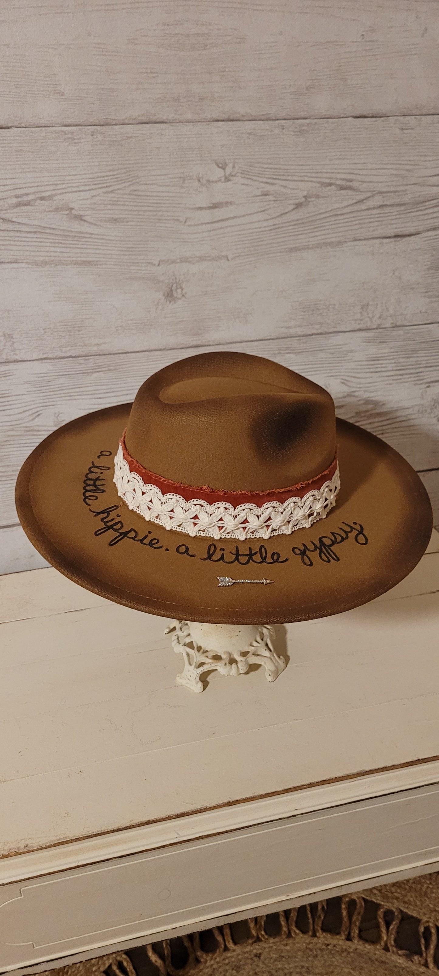 Features "a little hippie. a little gypsy." Natural lace ribbon, frayed velvet ribbon, rhinestone brooches: AB flowers, cactus & arrow Felt hat Flat brim 90% polyester & 10% PU Ribbon drawstring for hat size adjustment Head Circumference: 24" Crown Height: 5" Brim Length: 15.75" Brim Width: 14.5" Branded & numbered inside crown Custom burned & engraved by Kayla