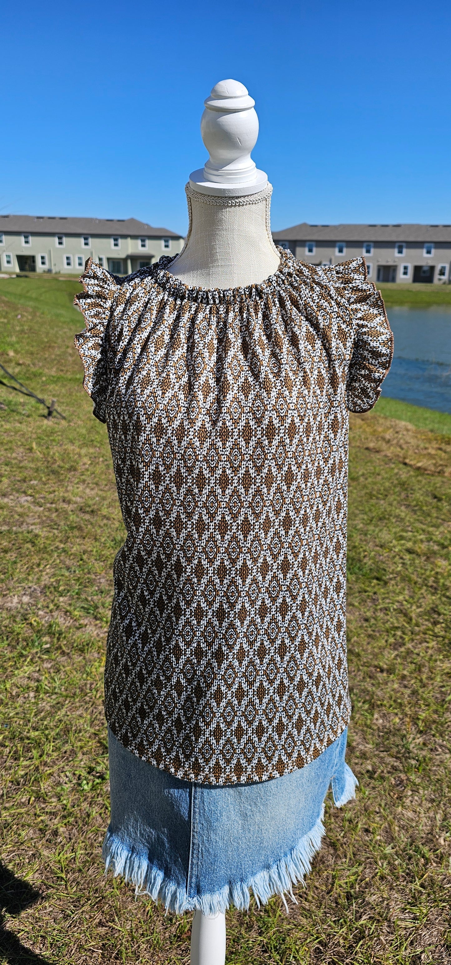 “Pretty Penny” is a patterned sleeveless blouse featuring a rounded hemline, a ruffled elastic neckline and ruffled sleeves. It is a waffle knit, relaxed fit. This is unlined, non-sheer, and lightweight. The colors are camel, white and black. Sizes small, medium and large