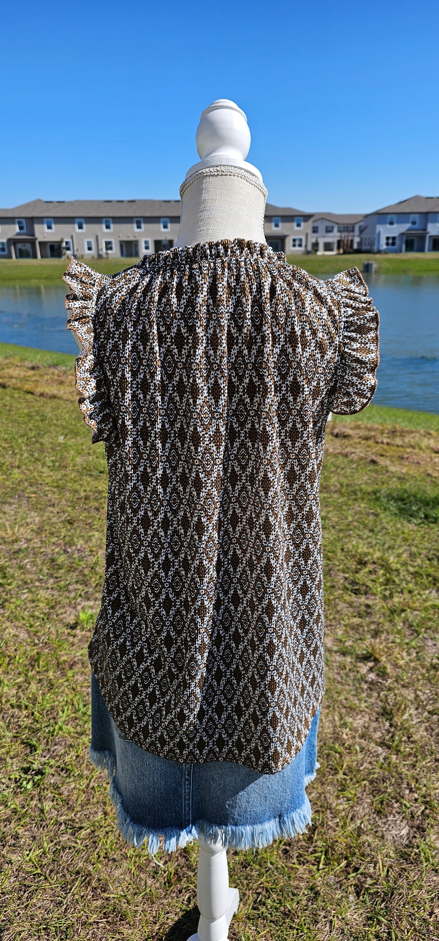 “Pretty Penny” is a patterned sleeveless blouse featuring a rounded hemline, a ruffled elastic neckline and ruffled sleeves. It is a waffle knit, relaxed fit. This is unlined, non-sheer, and lightweight. The colors are camel, white and black. Sizes small, medium and large