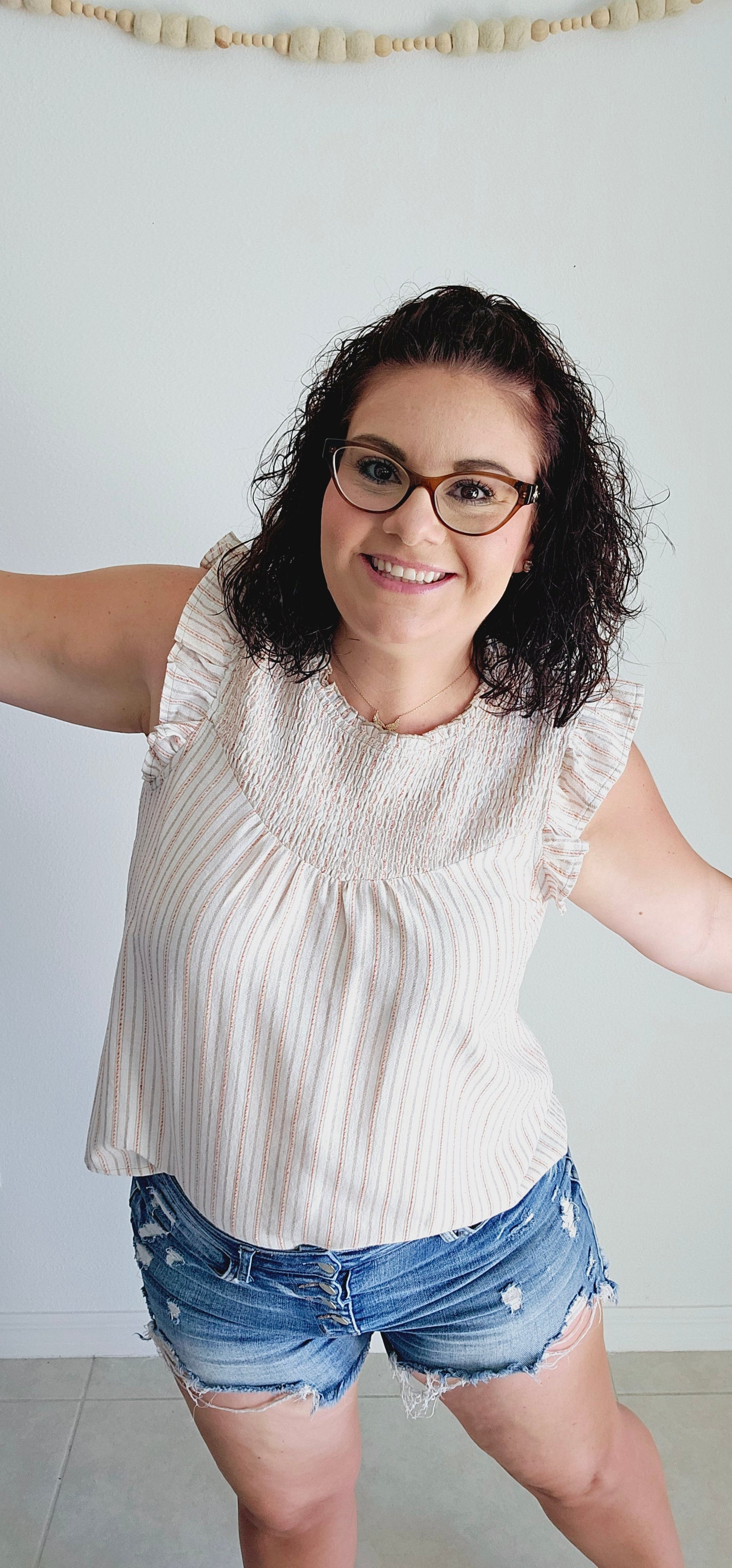 Add some fun to your wardrobe with this adorable blouse. Featuring a multi-color (taupe, mustard, red) stripe design, ruffle detail, and smocked chest, this sleeveless blouse is perfect for any occasion. Let your playful side shine through with this off white top! Sizes small through large.