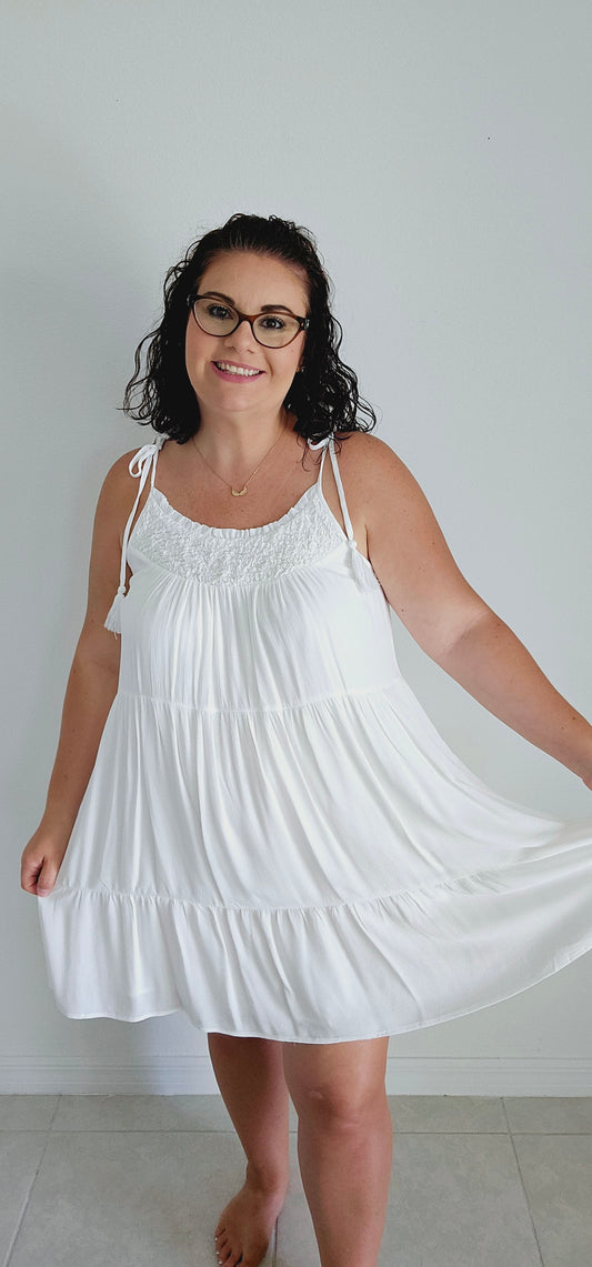 Get ready to make a statement with this flirty mini dress. Featuring a unique popcorn smocking chest and playful tassel detail straps, this dress is perfect for those vacation vibes. The tiered mini length adds a touch of fun and flirty to your look. Bring on the sun! Sizes small through large.