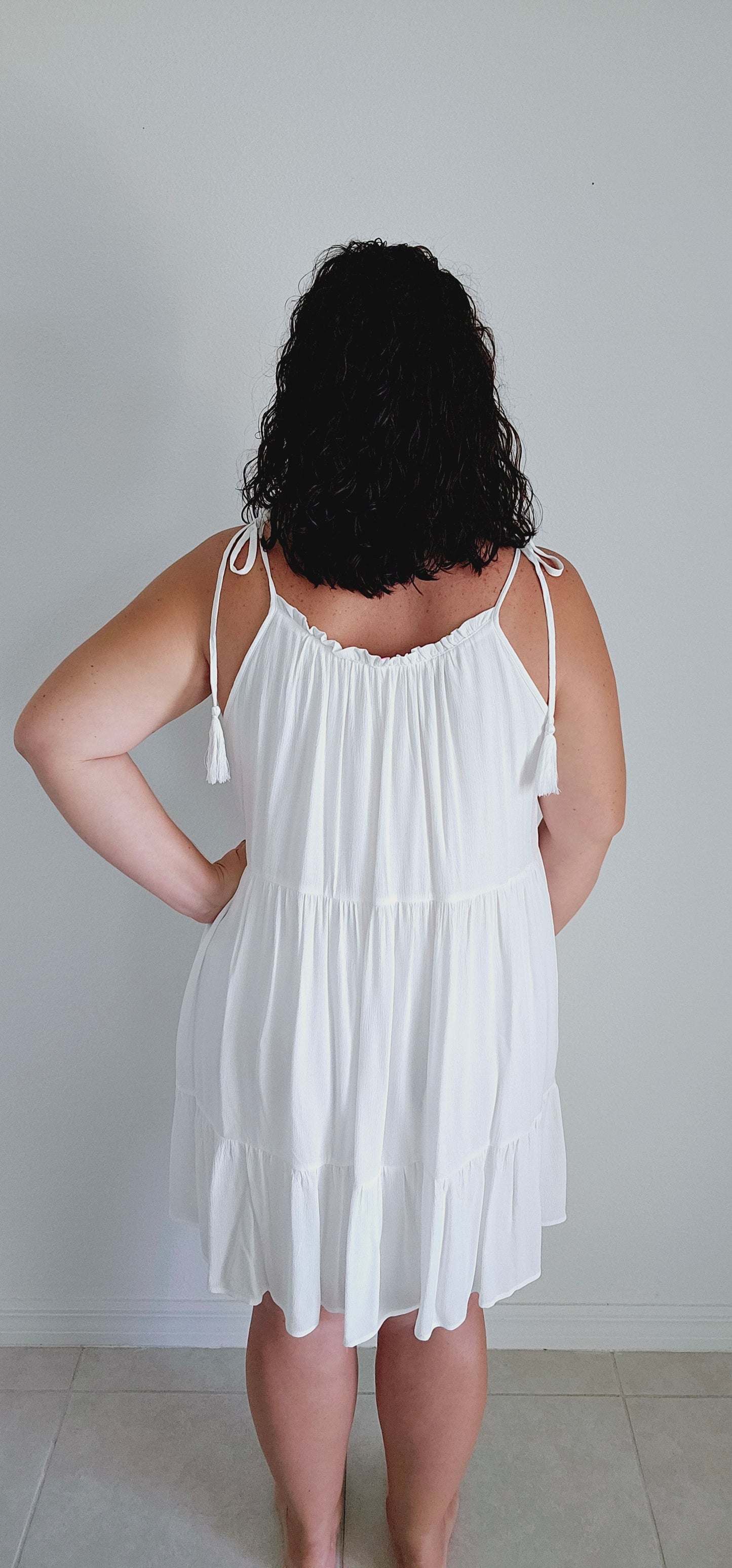 Get ready to make a statement with this flirty mini dress. Featuring a unique popcorn smocking chest and playful tassel detail straps, this dress is perfect for those vacation vibes. The tiered mini length adds a touch of fun and flirty to your look. Bring on the sun! Sizes small through large.