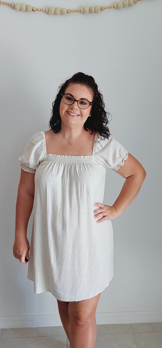 Be the queen of comfort and style in this adorable babydoll dress. With its smocked square neckline and puff short sleeves, this oatmeal-colored dress is perfect for any occasion. Its thigh length adds a flirty touch, making you feel confident and carefree. Don't miss out on this must-have dress! Sizes small through large.