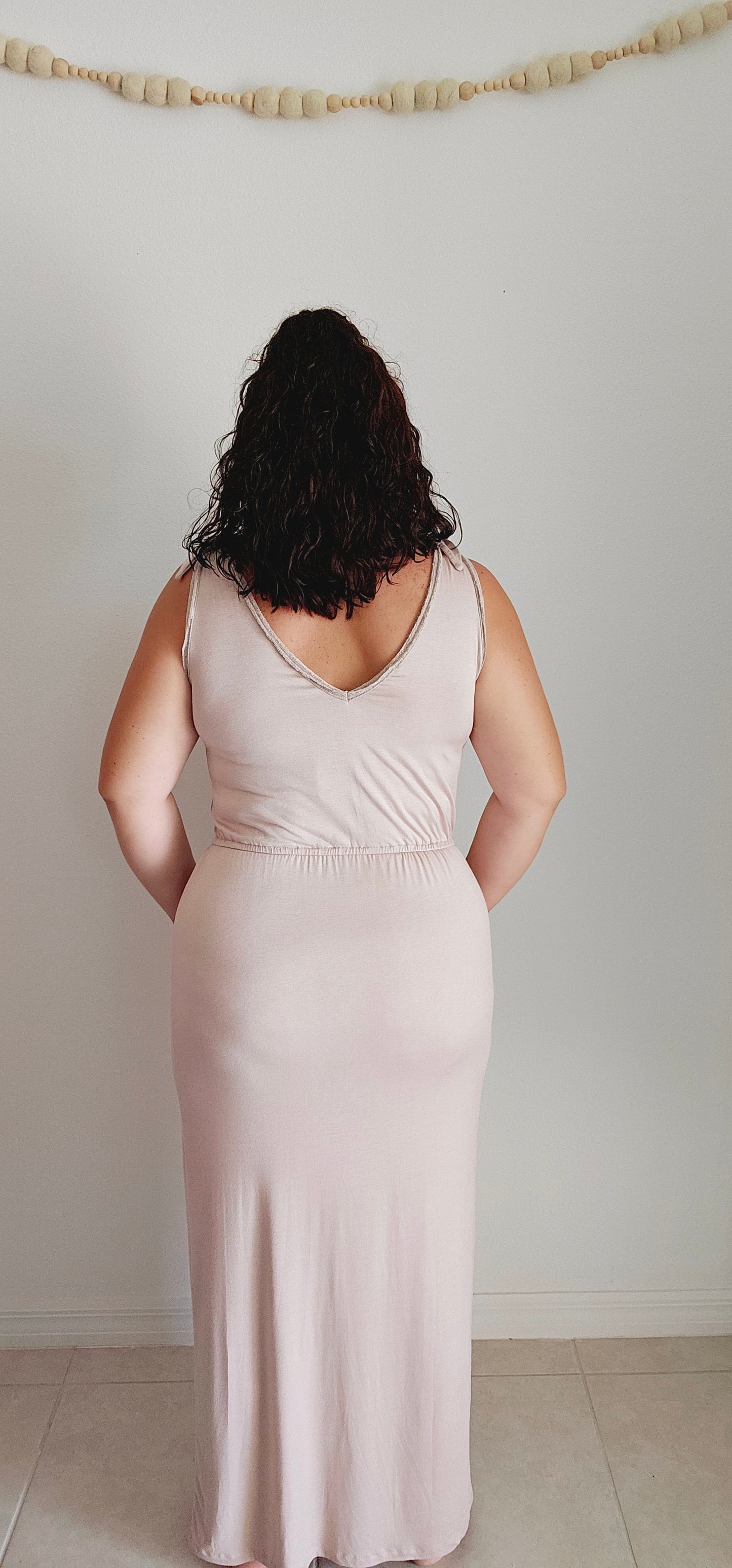Shake up your wardrobe with this modern maxi dress. The v-neck and v-back add a playful touch to this elegant piece. The elastic waist ensures a comfortable fit while the tie detail and fabric trim add some fun texture. Sizes small through large.
