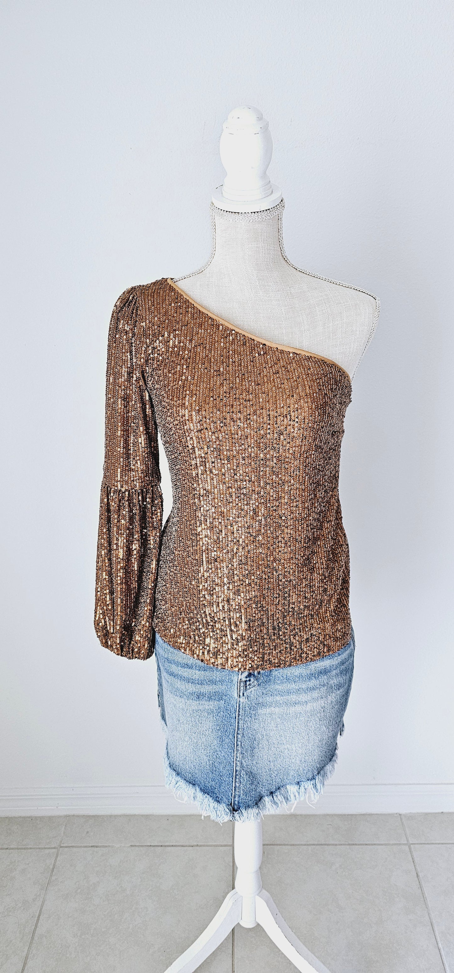 This gold sequined one shoulder top features a long puff sleeve, lining throughout, and side zipper with clasp. Pair with your favorite skirt or dress pants. Don’t be afraid to get creative! Sizes small through large.