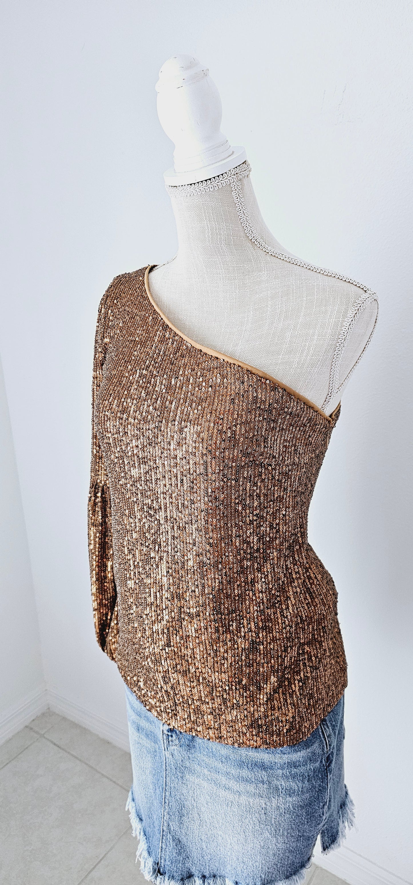This gold sequined one shoulder top features a long puff sleeve, lining throughout, and side zipper with clasp. Pair with your favorite skirt or dress pants. Don’t be afraid to get creative! Sizes small through large.