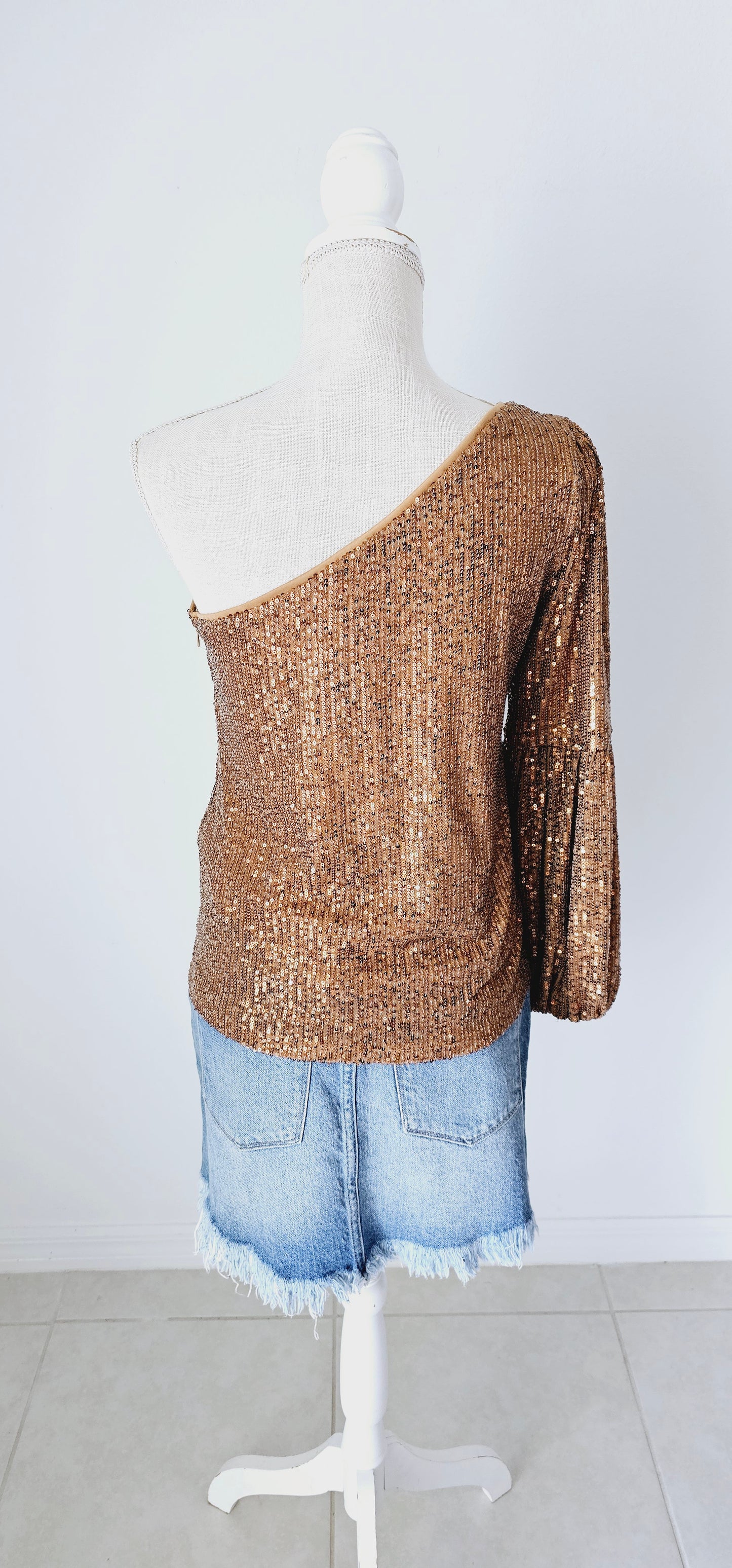 This gold sequined one shoulder top features a long puff sleeve, lining throughout, and side zipper with clasp. Pair with your favorite skirt or dress pants. Don’t be afraid to get creative! Sizes small through large.