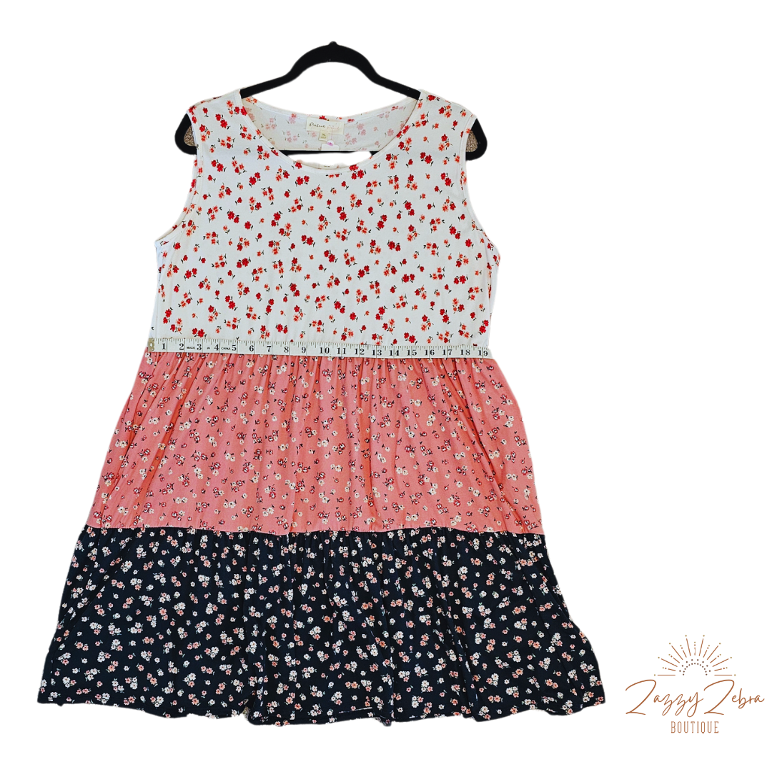 The “Flower Child“ dress is sleeveless, it features a rounded neckline, tiered layers, two functional pockets, and it sits above the knees. It is a buttery soft material. This is unlined, non-sheer, and lightweight. This dress is off white, dusty mauve, and navy blue with red, pink, and dusty mauve flowers. Sizes small through x-large.