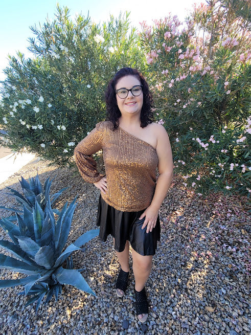 This gold sequined one shoulder top features a long puff sleeve, lining throughout, and side zipper with clasp. Pair with your favorite skirt or dress pants. Don’t be afraid to get creative! Sizes small through large.