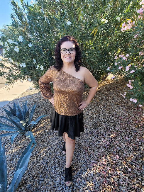 This gold sequined one shoulder top features a long puff sleeve, lining throughout, and side zipper with clasp. Pair with your favorite skirt or dress pants. Don’t be afraid to get creative! Sizes small through large.