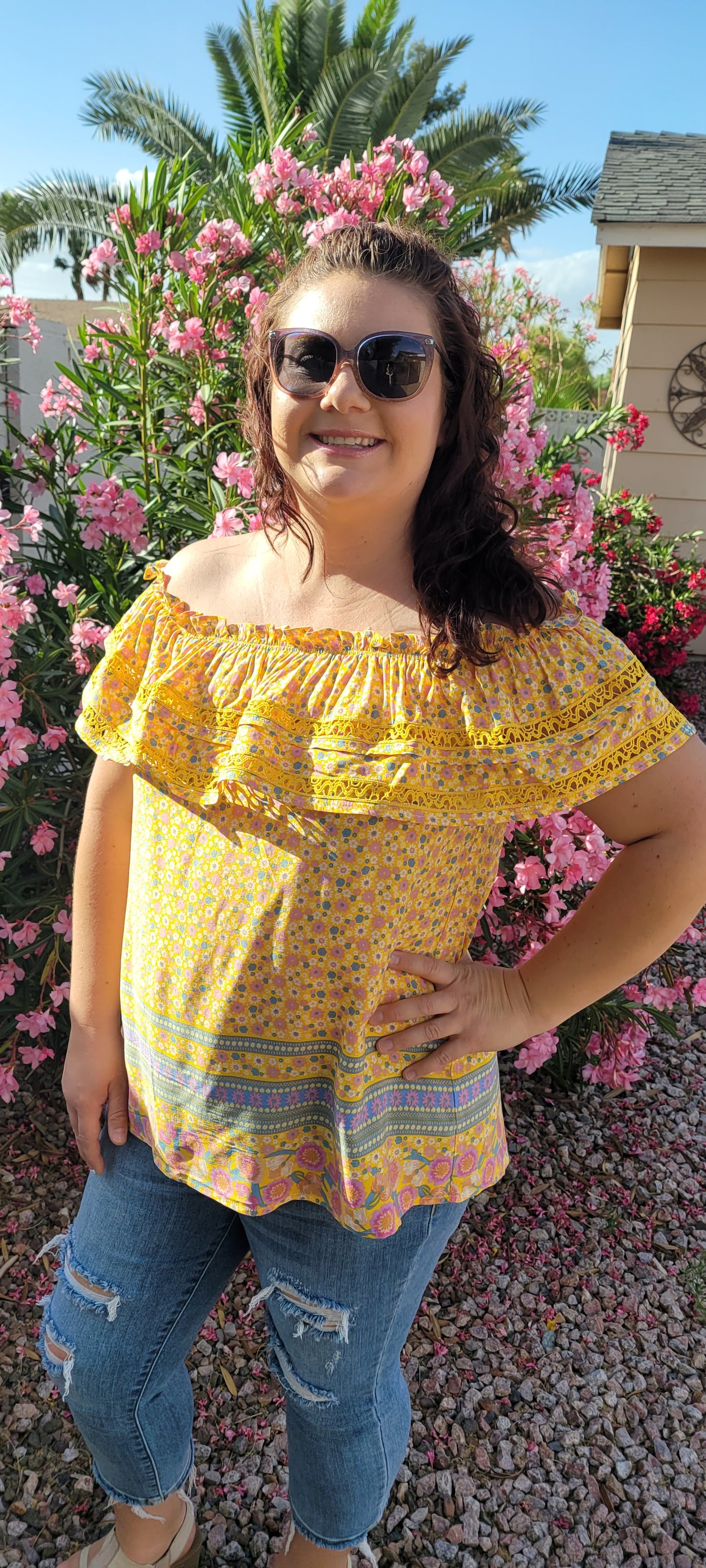 “Sunshine On My Shoulders” is an off the shoulder smock top. This top features a ray of subdued colors (dandelion yellow, mauve, ceil blue, white), elastic ruffled neckline, and crochet lace design. This top is a longer length, it does not have stretch, and is super lightweight and breathable. Sizes small through large.