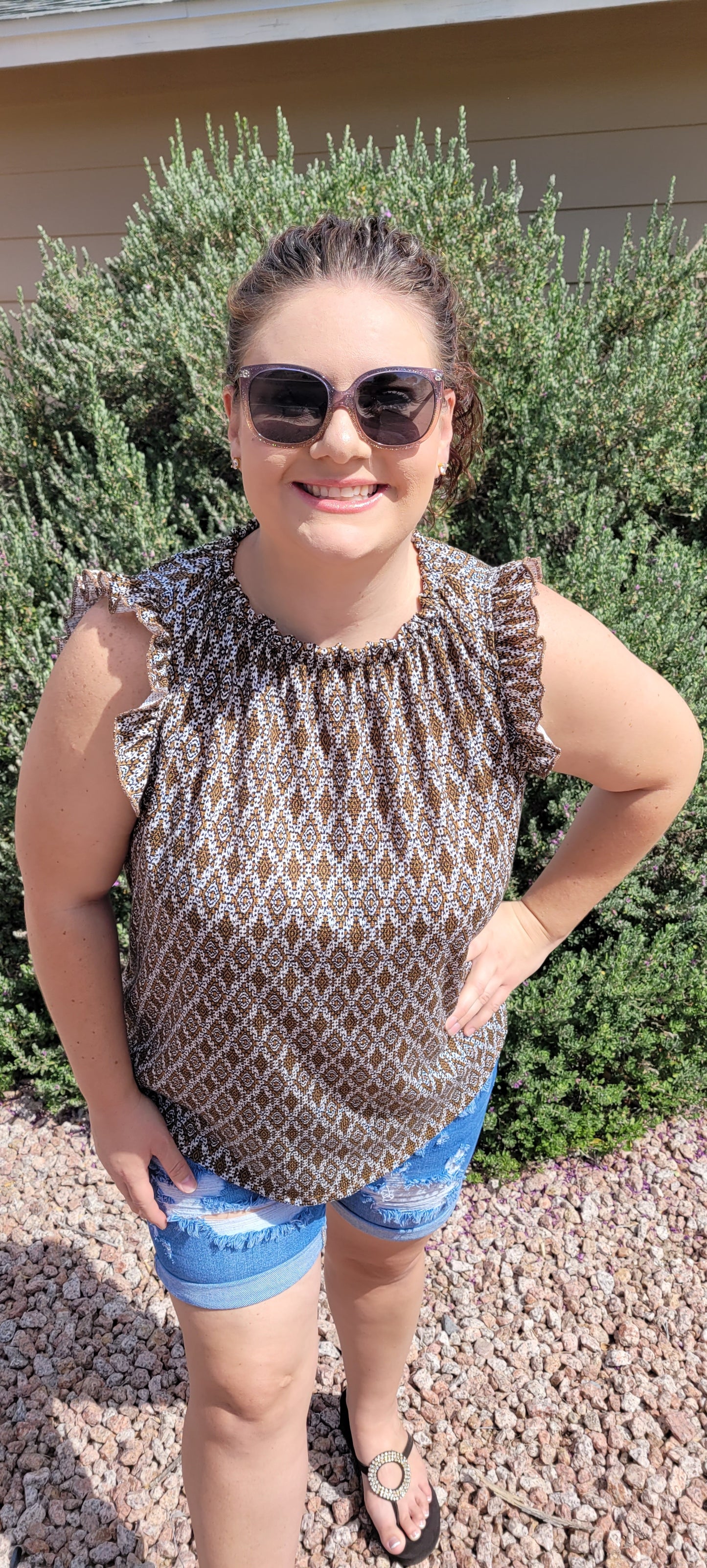 “Pretty Penny” is a patterned sleeveless blouse featuring a rounded hemline, a ruffled elastic neckline and ruffled sleeves. It is a waffle knit, relaxed fit. This is unlined, non-sheer, and lightweight. The colors are camel, white and black. Sizes small, medium and large