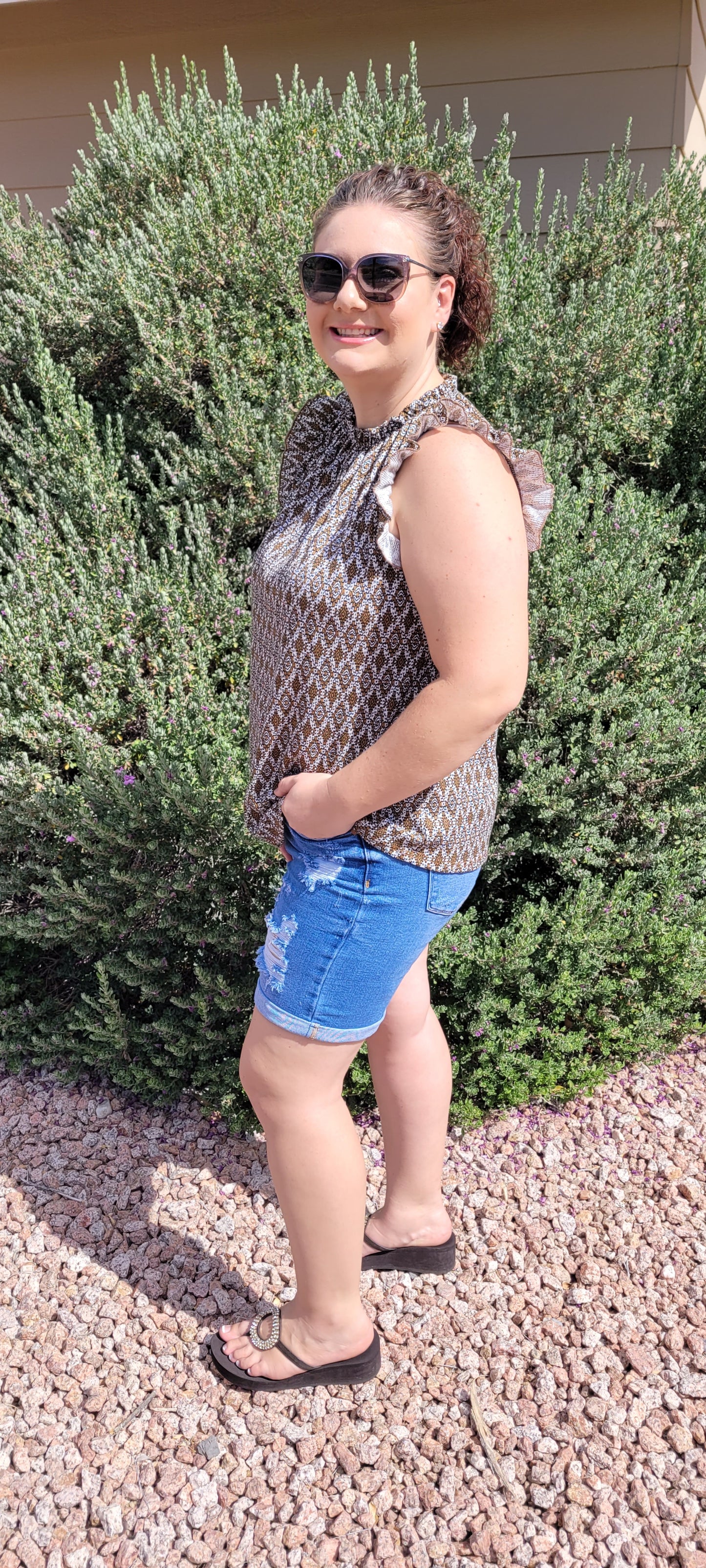 “Pretty Penny” is a patterned sleeveless blouse featuring a rounded hemline, a ruffled elastic neckline and ruffled sleeves. It is a waffle knit, relaxed fit. This is unlined, non-sheer, and lightweight. The colors are camel, white and black. Sizes small, medium and large