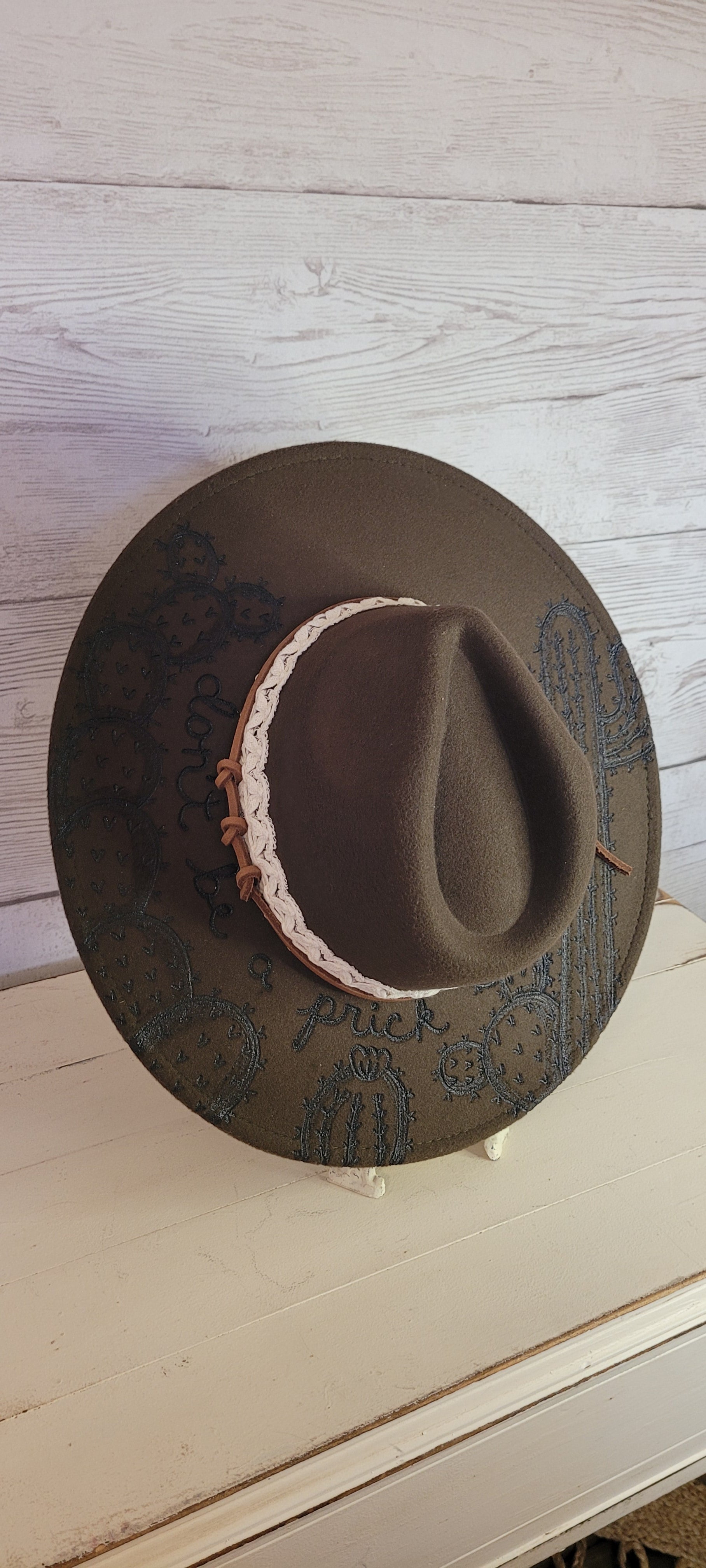 Features "don't be a prick", cactus & saguaro engraving Natural lace ribbon & leather band Felt hat Flat brim 65% polyester and 35% cotton Ribbon drawstring for hat size adjustment Head Circumference: 24" Crown Height: 5" Brim Length: 15.75" Brim Width: 14.5" Branded & numbered inside crown Custom designed by Kayla
