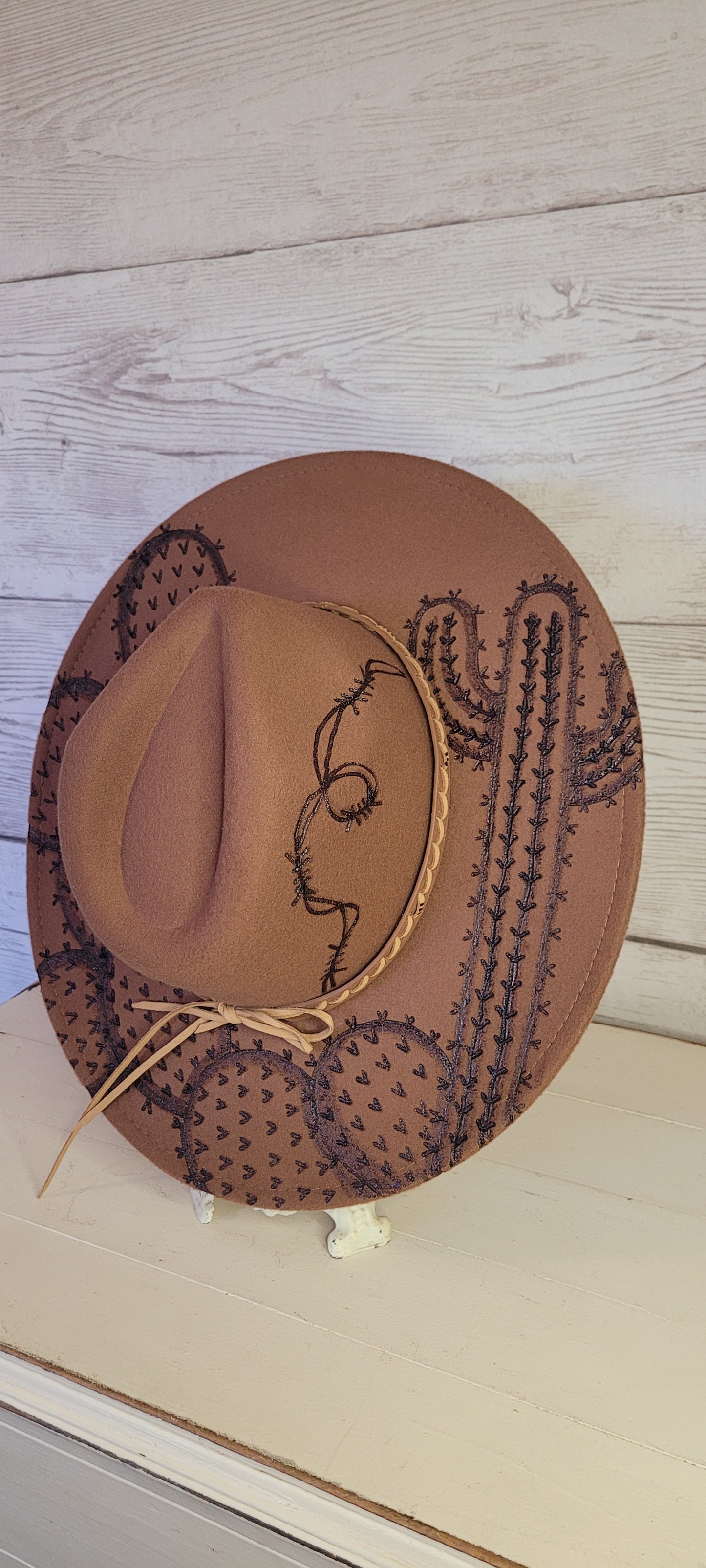 Features barbwire, cactus & saguaro Natural lace ribbon & leather band Felt hat Flat brim 100% polyester Ribbon drawstring for hat size adjustment Head Circumference: 24" Crown Height: 5" Brim Length: 15.75" Brim Width: 14.5" Branded & numbered inside crown Custom engraved by Kayla