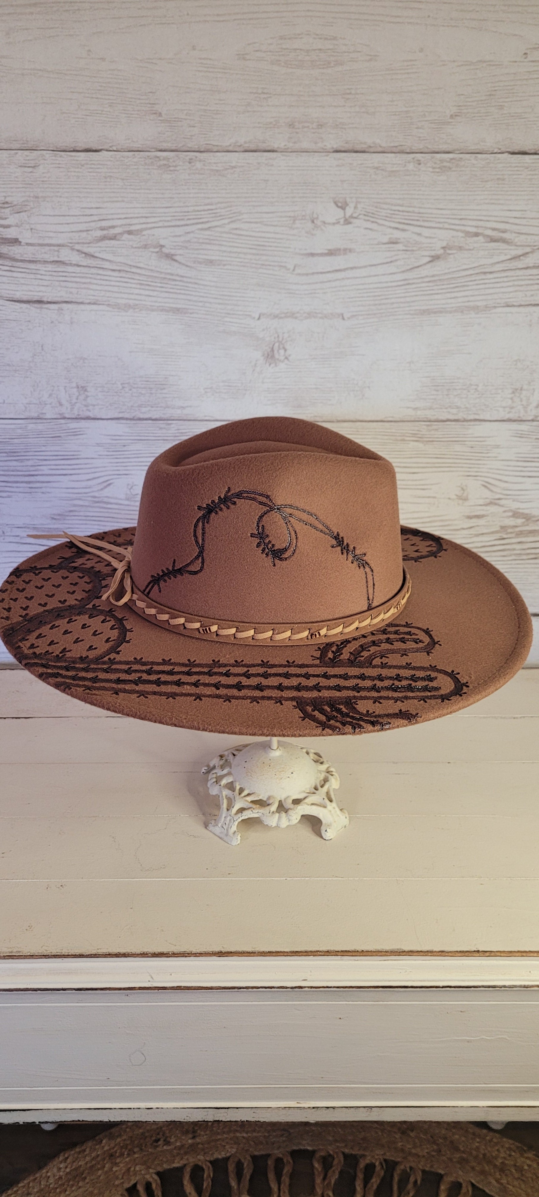 Features barbwire, cactus & saguaro Natural lace ribbon & leather band Felt hat Flat brim 100% polyester Ribbon drawstring for hat size adjustment Head Circumference: 24" Crown Height: 5" Brim Length: 15.75" Brim Width: 14.5" Branded & numbered inside crown Custom engraved by Kayla