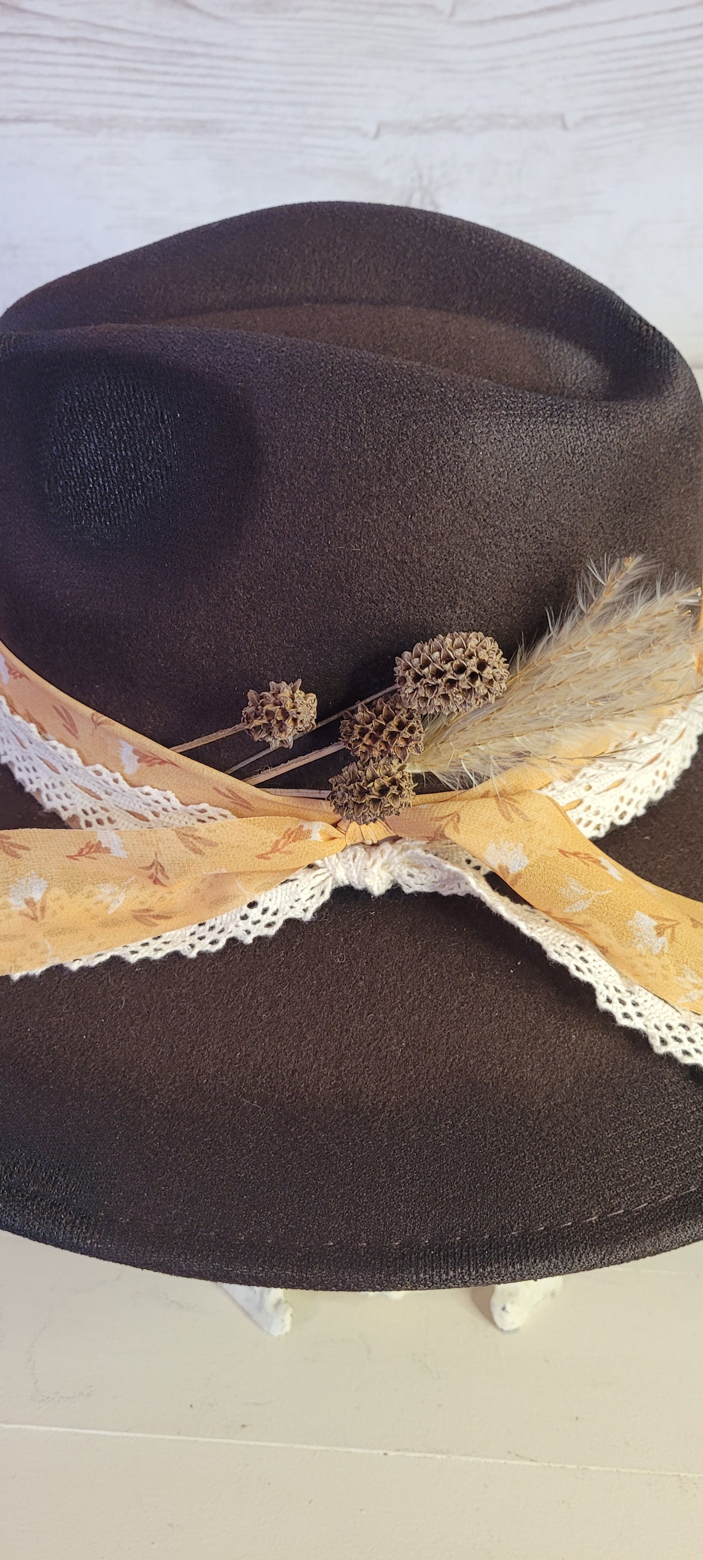 Features natural lace ribbon, sheer mustard ribbon, pine cones, & pampas Felt hat Flat brim 65% polyester and 35% cotton Ribbon drawstring for hat size adjustment Head Circumference: 24" Crown Height: 5" Brim Length: 15.75" Brim Width: 14.5" Branded & numbered inside crown Custom designed by Kayla