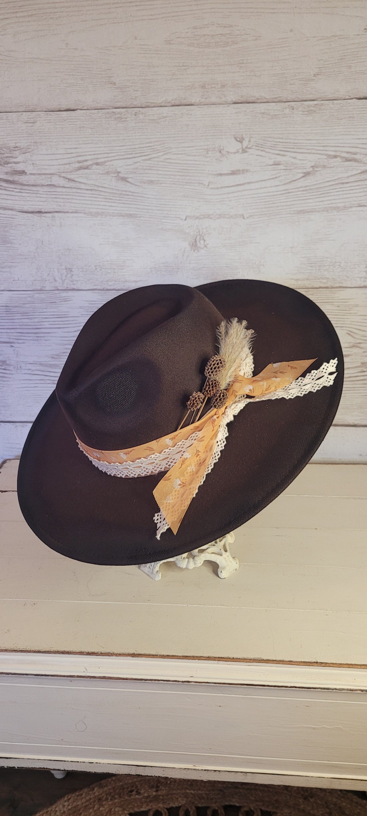 Features natural lace ribbon, sheer mustard ribbon, pine cones, & pampas Felt hat Flat brim 65% polyester and 35% cotton Ribbon drawstring for hat size adjustment Head Circumference: 24" Crown Height: 5" Brim Length: 15.75" Brim Width: 14.5" Branded & numbered inside crown Custom designed by Kayla