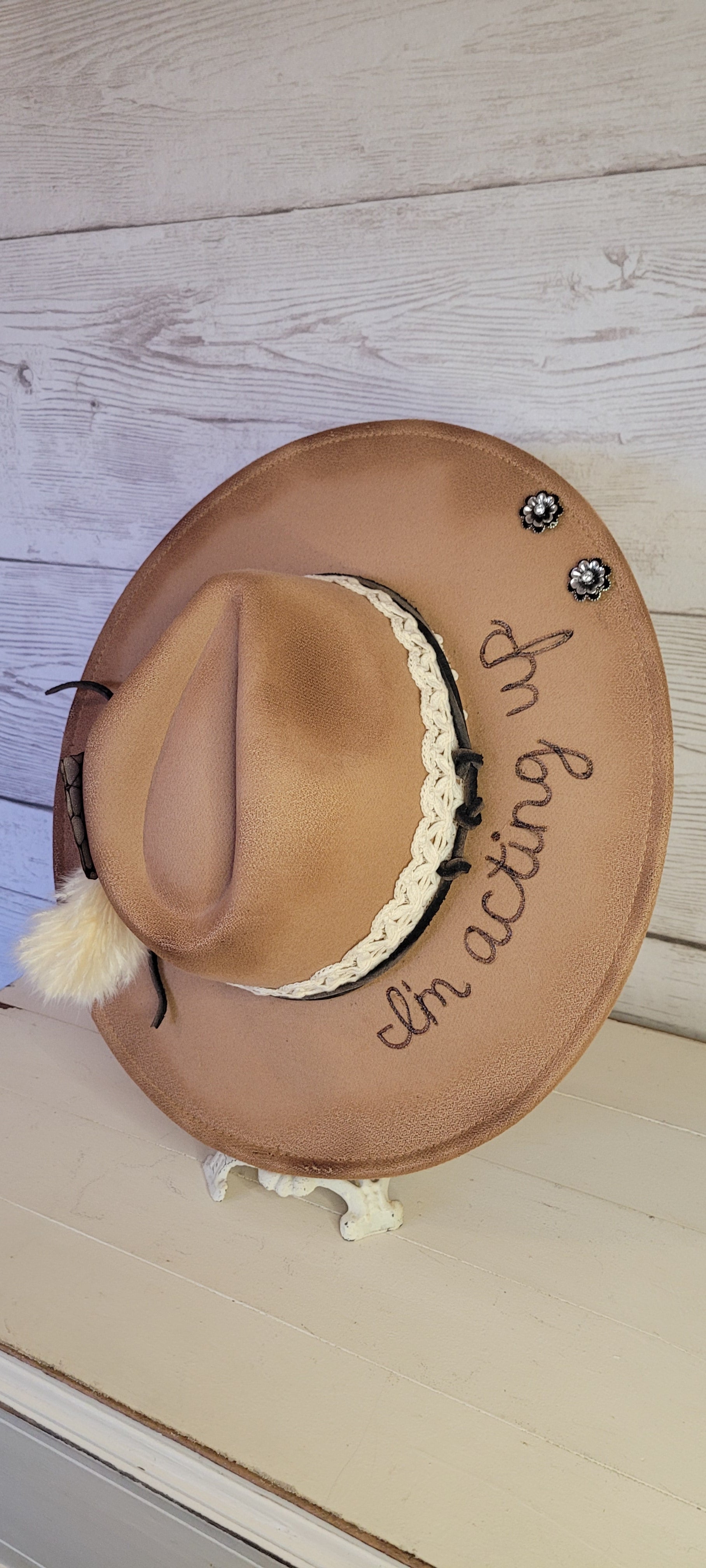 Features "I'm acting up" engraving Lace ribbon, leather band, pampas, rhinestone brooches, playing card Felt hat Flat brim 100% polyester Ribbon drawstring for hat size adjustment Head Circumference: 24" Crown Height: 5" Brim Length: 15.75" Brim Width: 14.5" Branded & numbered inside crown Custom burned & engraved by Kayla