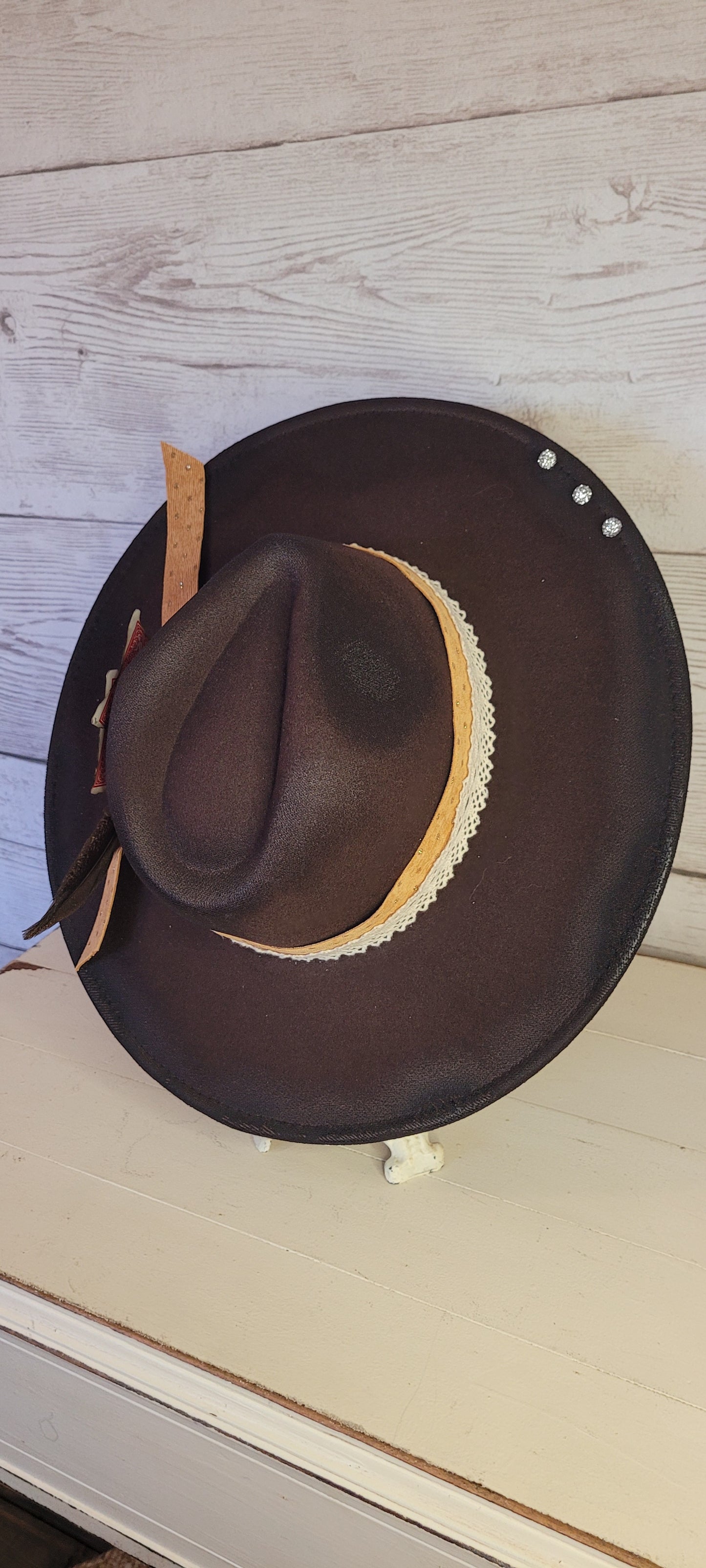 Features natural lace ribbon, corduroy ribbon, feather, playing cards, pistol brooch, & rhinestone beads Felt hat Flat brim 65% polyester and 35% cotton Ribbon drawstring for hat size adjustment Head Circumference: 24" Crown Height: 5" Brim Length: 15.75" Brim Width: 14.5" Branded & numbered inside crown Custom designed by Kayla