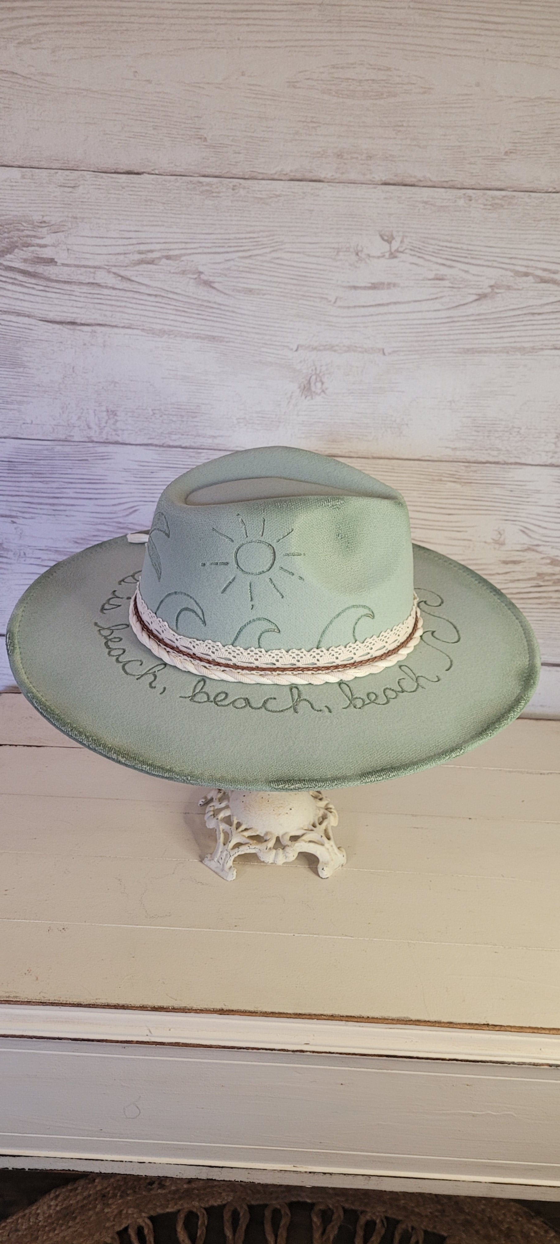 Features sunshine, palm trees, waves & "all she does is beach, beach, beach" engraved Lace ribbon, brown cord, & natural gauze rope Felt hat Flat brim 65% polyester and 35% cotton Ribbon drawstring for hat size adjustment Head Circumference: 24" Crown Height: 5" Brim Length: 15.75" Brim Width: 14.5" Branded & numbered inside crown Custom burned & engraved by Kayla