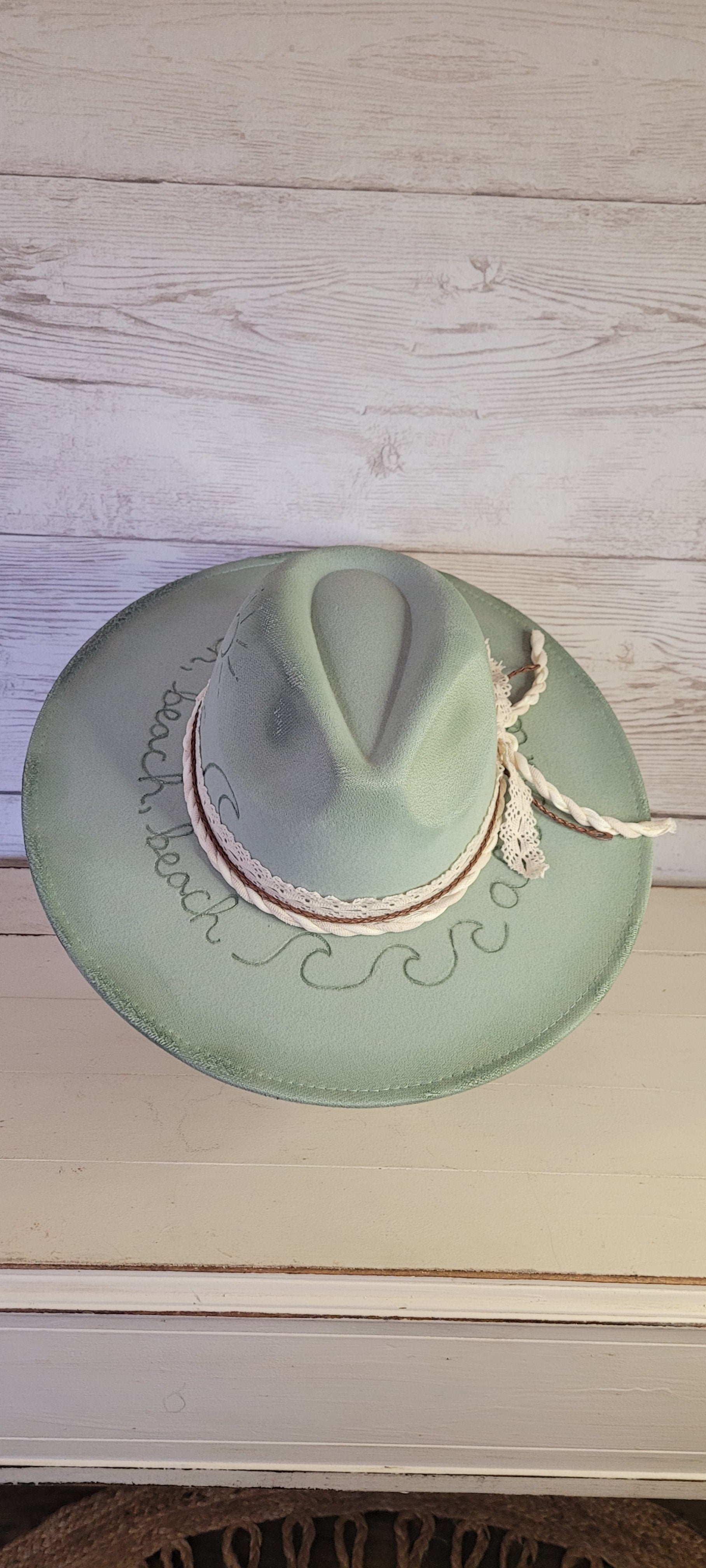Features sunshine, palm trees, waves & "all she does is beach, beach, beach" engraved Lace ribbon, brown cord, & natural gauze rope Felt hat Flat brim 65% polyester and 35% cotton Ribbon drawstring for hat size adjustment Head Circumference: 24" Crown Height: 5" Brim Length: 15.75" Brim Width: 14.5" Branded & numbered inside crown Custom burned & engraved by Kayla