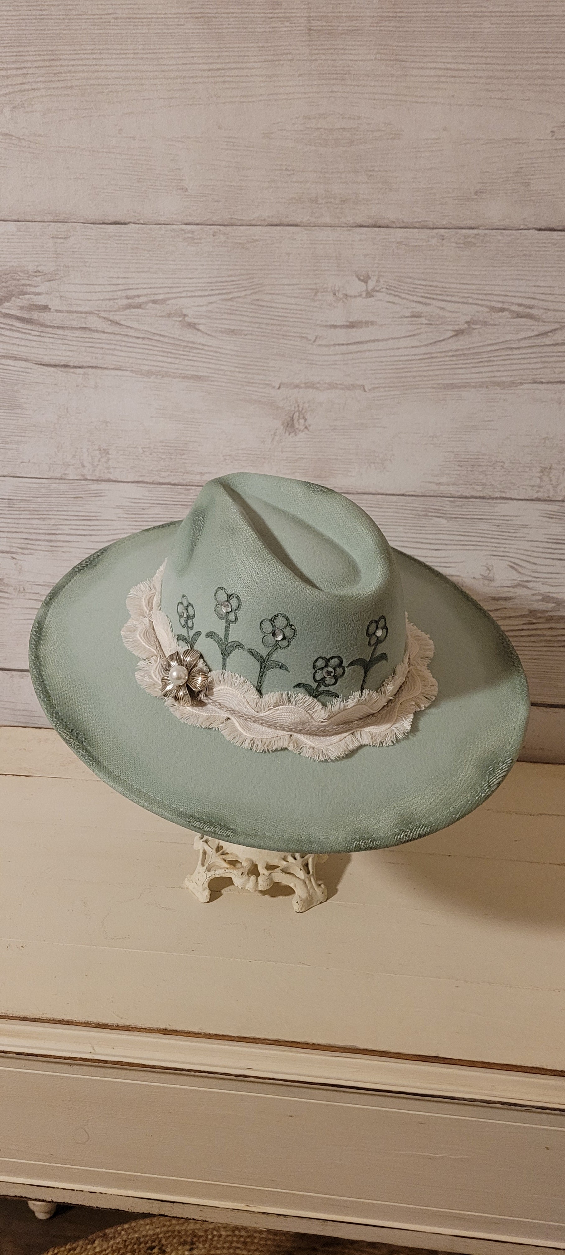 Features flowers engraved Wavy frayed ribbon, natural cord, rhinestones & metal pearl brooch Felt hat Flat brim 100% polyester Ribbon drawstring for hat size adjustment Head Circumference: 24" Crown Height: 5" Brim Length: 15.75" Brim Width: 14.5" Branded & numbered inside crown Custom burned & engraved by Kayla