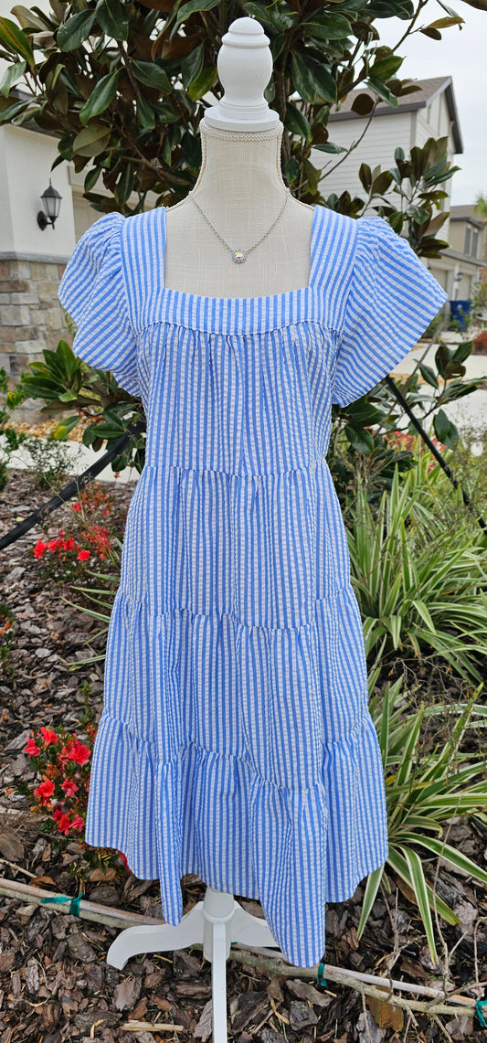 “Not In Kansas” dress features a square neckline and backline, ruffled sleeves, tiered and pleated layers, and a rounded hemline. This white and baby blue striped dress sits at the knees. This is a woven, seersucker fabric, breathable, non-stretch fabric, unlined, non-sheer, and lightweight. This dress is perfect for a beach getaway! Sizes small through large.