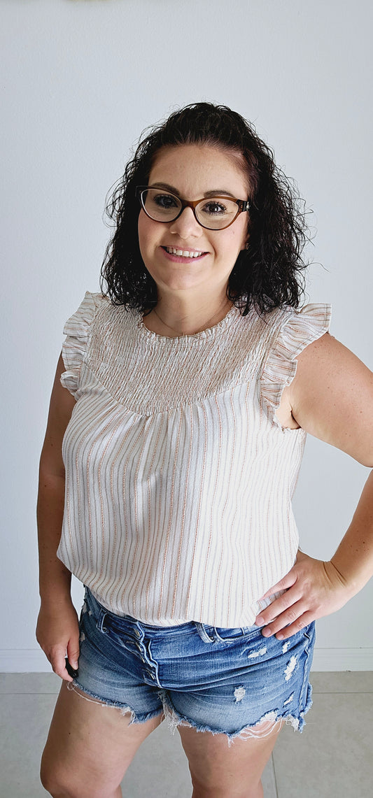 Add some fun to your wardrobe with this adorable blouse. Featuring a multi-color (taupe, mustard, red) stripe design, ruffle detail, and smocked chest, this sleeveless blouse is perfect for any occasion. Let your playful side shine through with this off white top! Sizes small through large.