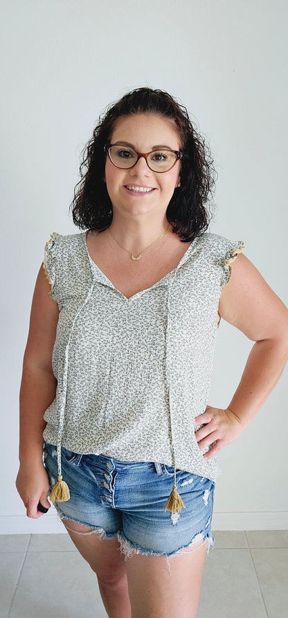 This fun and flirty blouse features a playful ditsy floral pattern and charming scalloped mustard trim. The ruffle sleeves add a touch of whimsy, while the tie closure with mustard tassels offers a unique and stylish detail. Perfect for a quirky and playful look. Sizes small through large.