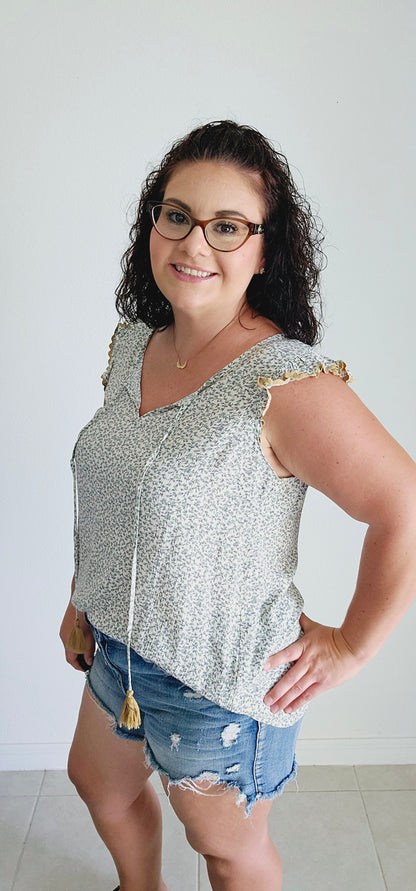 This fun and flirty blouse features a playful ditsy floral pattern and charming scalloped mustard trim. The ruffle sleeves add a touch of whimsy, while the tie closure with mustard tassels offers a unique and stylish detail. Perfect for a quirky and playful look. Sizes small through large.